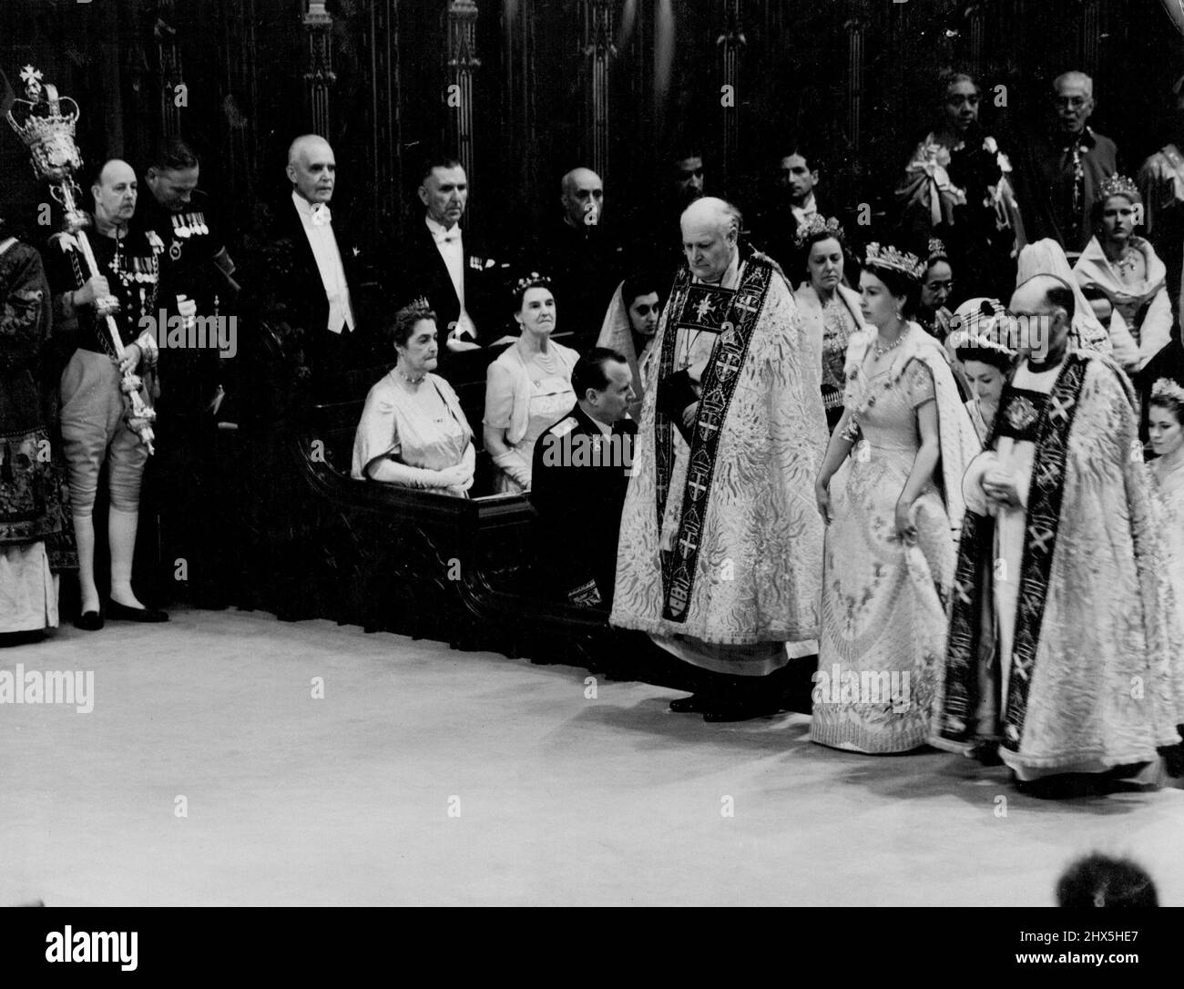 Coronation: The Queen In The Abbey The Queen during her progress through Westminster Abbey after her arrival for the Coronation ceremony to-day (Tuesday). On either side of the Queen are the Bishop of Durham, the Rt. Rev. Arthur Michael Ramsay (left) and the Bishop of Bath and Wells, the Rt. Rev. Harold William Bradfield. The Queen is wearing her Royal robe of crimson velvet, trimmed with ***** and bordered with gold lace. On her head, she has a diadem of precious stones. The Queen is also wearing the collar of the Garter. June 2, 1953. (Photo by Reuterphoto). Stock Photo
