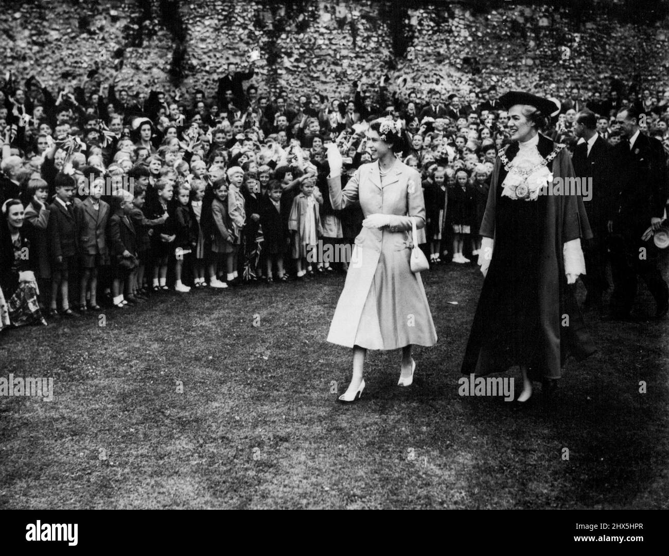 The Queen waves to school- ***** greet her at Pilgrim's School, Playing Field ***** Monday. Beside her walks Councillor *****. July 26, 1955. (Photo by Evening Standard Picture). Stock Photo