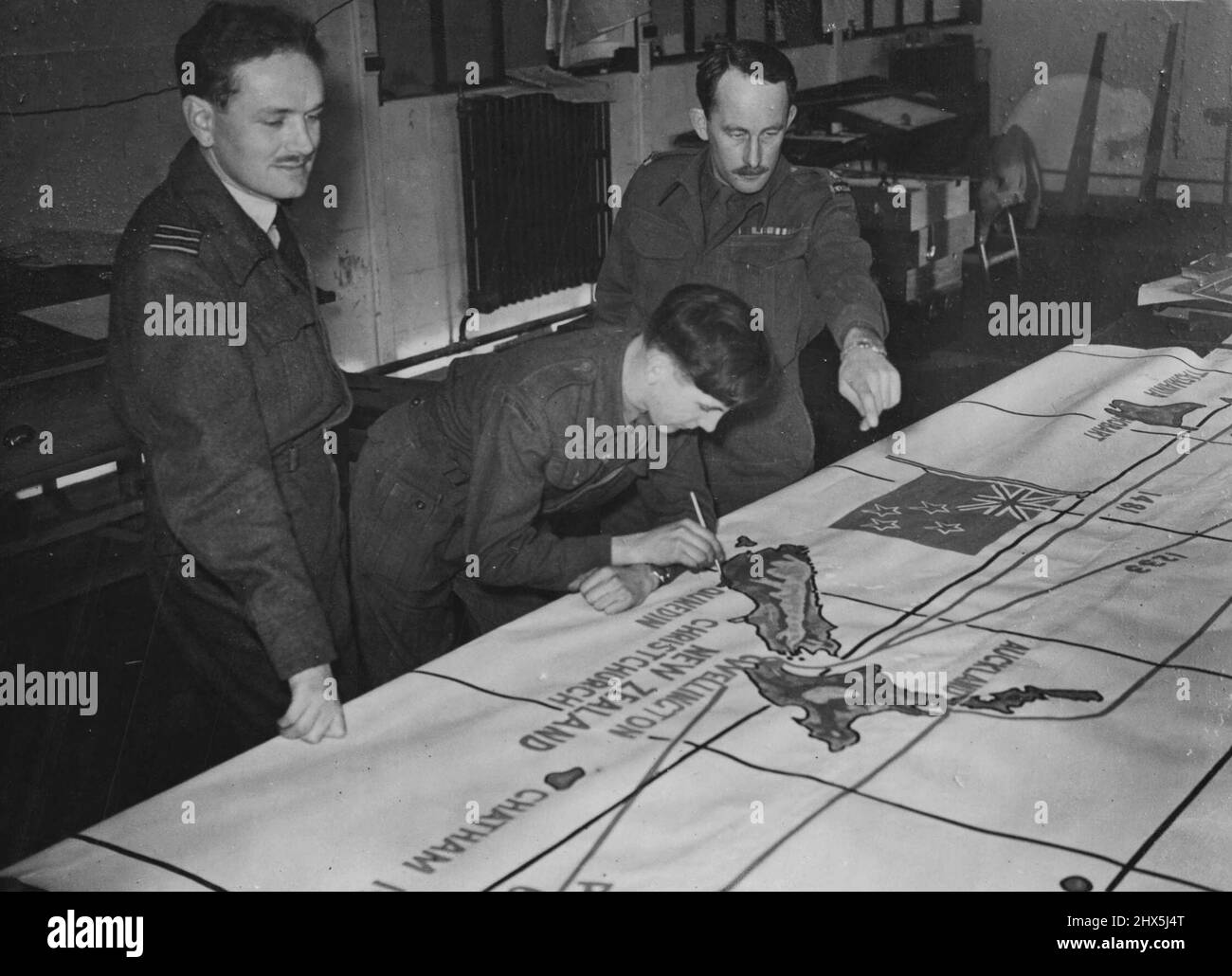 New Zealand Officers At Joint Services Staff College -- Wing Commander T.F. Gill, of Wellington, New Zealand (left) and Major B.R. Bullot, of Wellington, New Zealand (right) watching Private D. Howell, R.O.C. London at work painting a large-scale map, at the Joint Services Staff College. At the Joint Services Staff College, at Latimer, Chesham, Buckinghamshire, which is administered by the War office, officers of the combined services - the Navy, Army, and Air Force, are trained for appointments on joint Staffs, and to develop mutual understanding and a common doctrine between the Services, Stock Photo