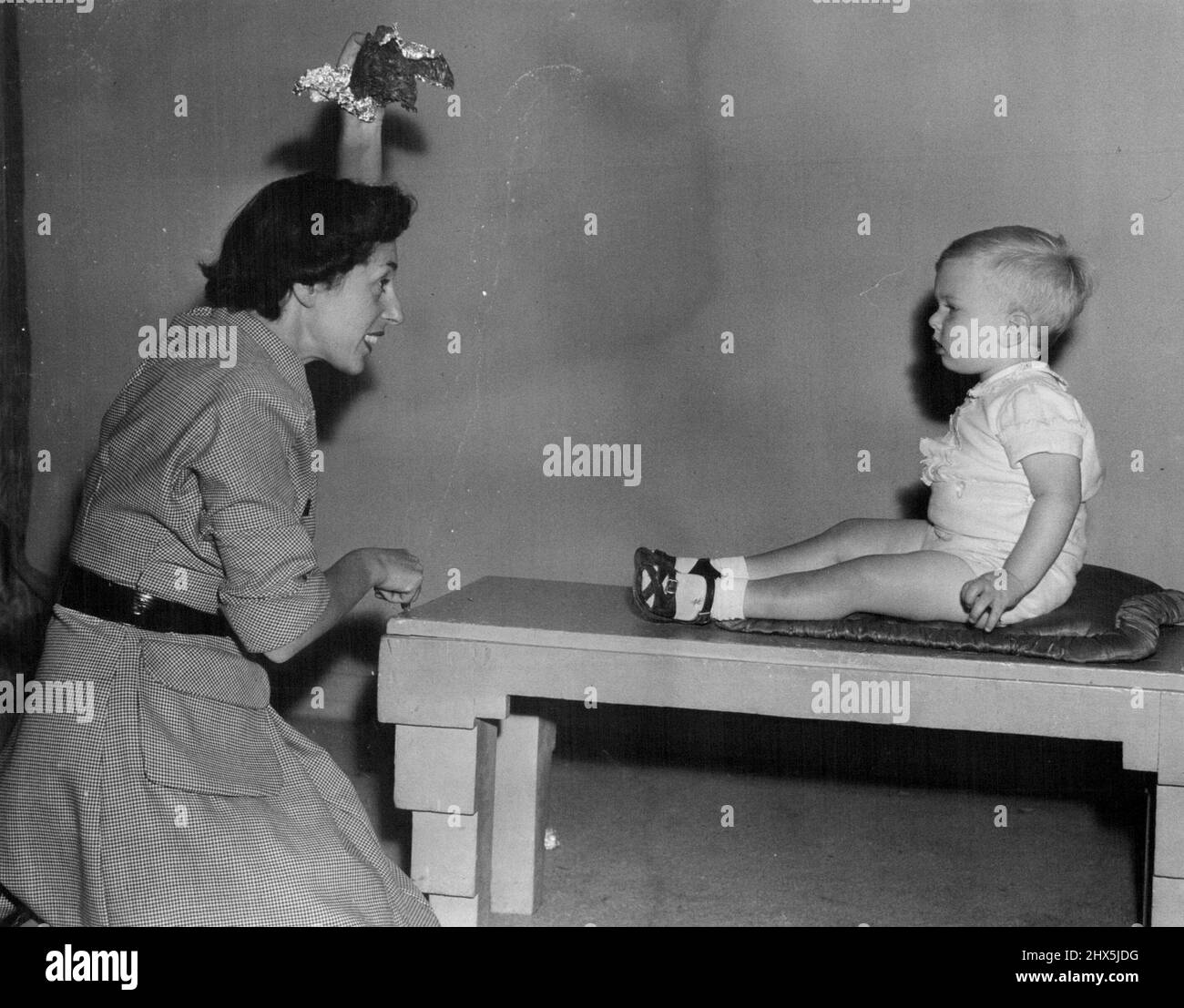 Shmith's sister, Verna, uses no toys to cajole young sitters but a natural sense of fun. Her brother watches carefully for the picture. May 24, 1950. Stock Photo