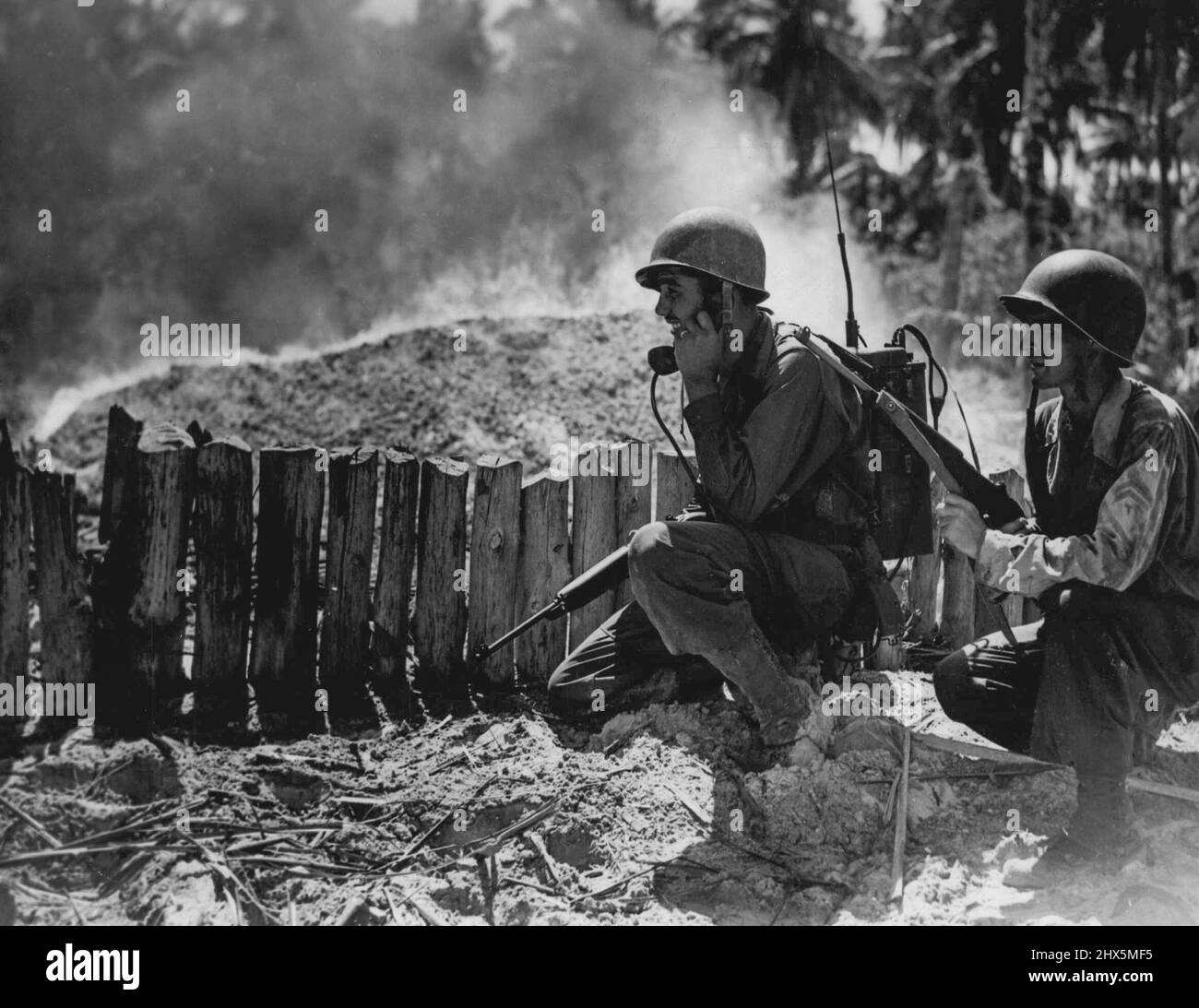 Sgt. O. De Giraloms, Ohio left and Private R. B. Cox, Washington D.C. right immediately contact the second landing party after reaching the beach at Morotai. Note the Japanese dump blazing in the background. September 23, 1944. Stock Photo
