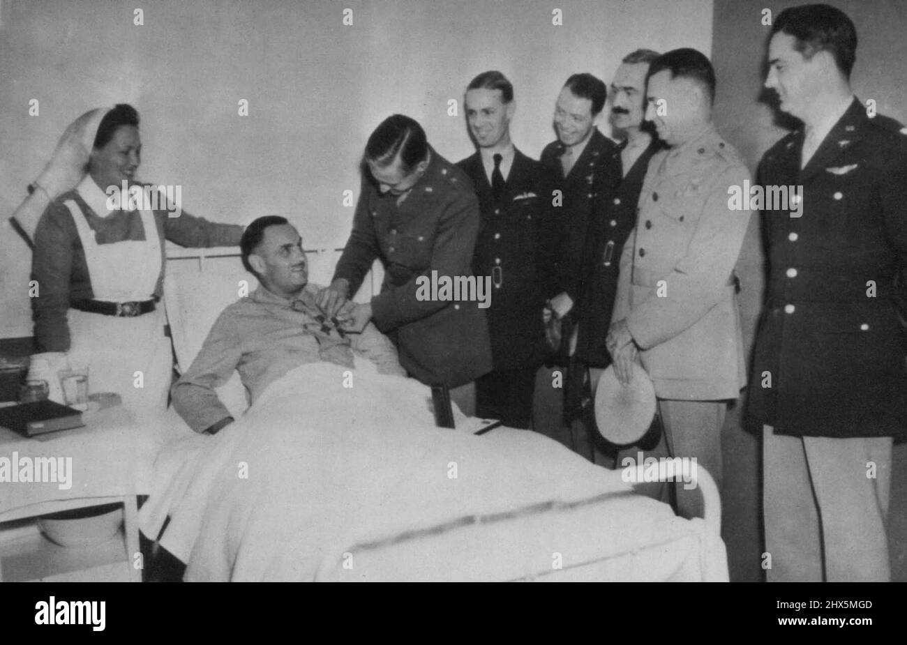 Lying on hospital bed at a Canadian Army base some where in the United Kingdom, Lieut. Col. Loren B. Hillsinger of New York receives distinguished service cross and order of the purple heart from Brig. Gen. L.K.Truscott Jr. for his valor in the dieppe raid, where he lost a leg. Other officers right to left are Lt. Col. D. E. Williams, Col. H. D. Campbell, Brig, F. O'D. Hunter, Brig. Gen. H.A. Craid, and group captain A. H. Willetts of the RAF. nurse is Andree Dalton, of Prince Edward island, Canada. September 20, 1942. (Photo by AP Wirephoto). Stock Photo