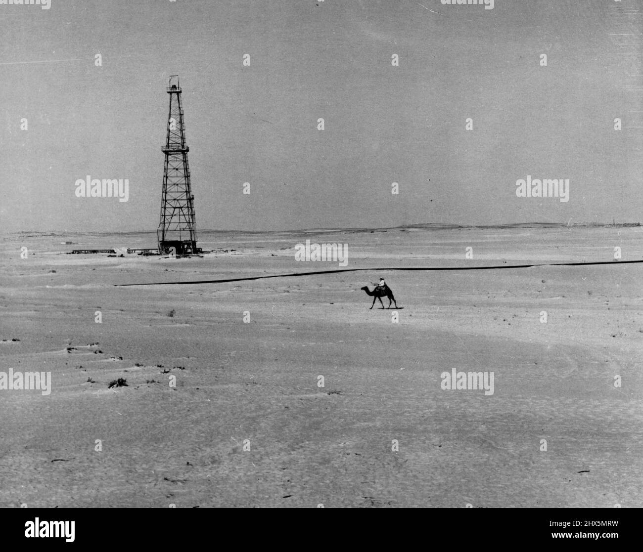 ***** Saudi Arabia...downstream development within the ***** ***** and rider, ancient ***** life, pass a modern derrick and oil ***** line in sandy wastes near Abqaiq, Saudi Arabia. Operations in Saudi Arabia ***** by the Arabian American oil Co. *****. December 14, 1955. Stock Photo