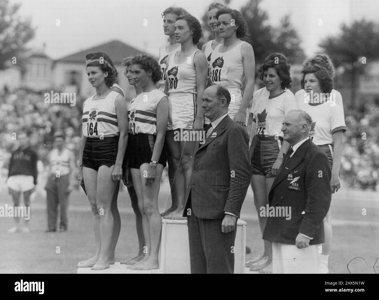 Empire Games Athletics, Final Day, Eden Park, Auckland -- On the Victory Stand after the women's 660 yards relay. The winners (Australia), centre, comprise V. Johnston, A. Shanley, M. Jackson and S. Strickland. England (second) comprise M. Walker, D.G. Manley, S. Cheeseman and D. Batter. Canada (third) comprise E. Silburn, G. Bemister, E. McKenzie and P. Jones. June 14, 1950. (Photo by The N.Z. Herald). Stock Photo