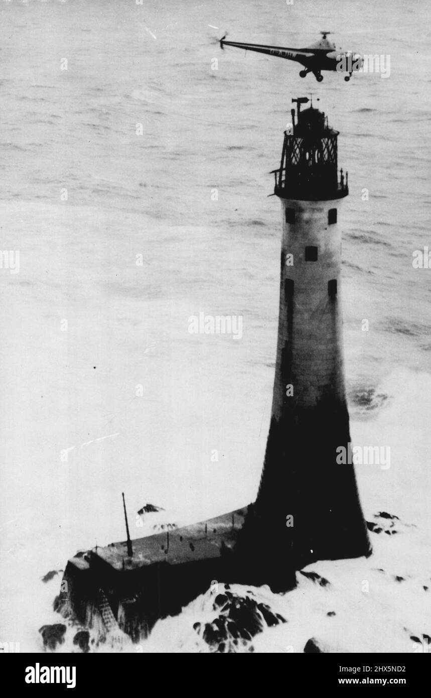 Helicopter Relieves Wolf Rock - A dramatic picture as the Helicopters hovers over the Wolf Rock lighthouse while the heavy seas surge around the base of the light-house as the food and mail are lowered to the three men on the lighthouse. Wolf Rock lighthouse, off Land's End, cut off by raging Atlantic seas for the past 26 days, was relieved yesterday - by helicopter. Guided by a circling naval aircraft, the blue and silver Trinity House helicopter, piloted by Captain Alan Bristow, approached the 135-ft, high tower and lowered three bags of food and mail to the occupants on the lamp balcony. Stock Photo