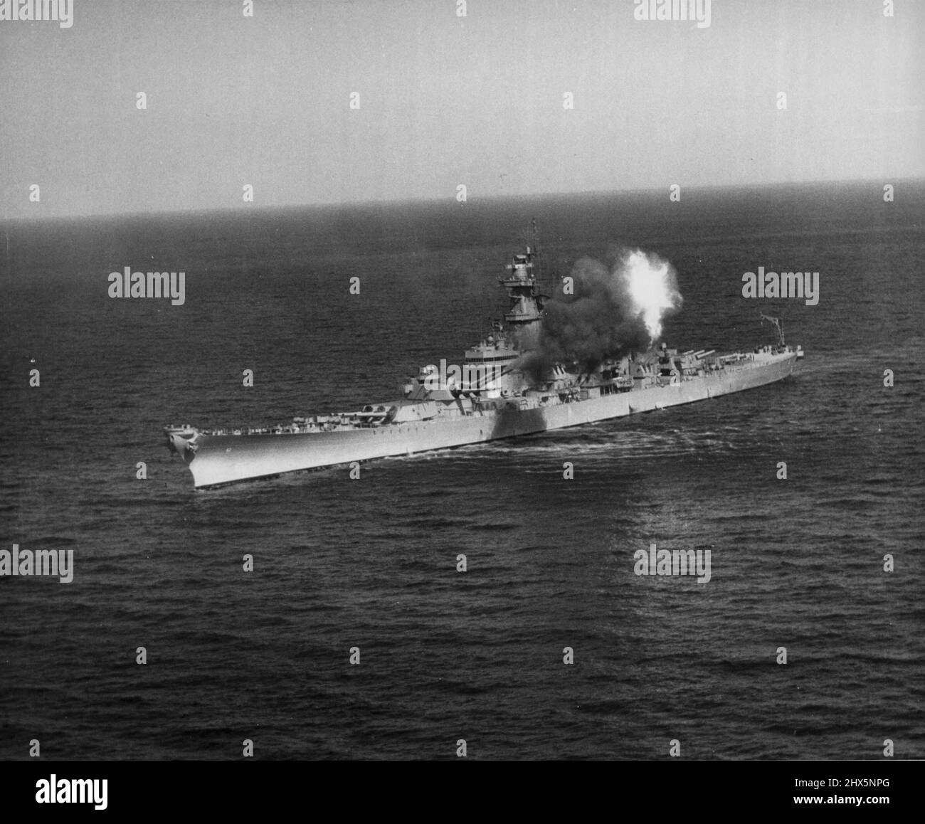 Battleship New CVR LY Blasts Chinese ***** - Navy combat cameramen climbed in a helicopter and hevered near the powerful battlewagon USS New Jersey to get this picture as she sent a salvo of 16-inch gun fury screaming toward Chinese Red strategic supply and transportation points along the east Korean coast. New Jersey is one of the largest and rest powerful fighting ship in existence today. June 06, 1951. (Photo by Official U S Navy Photograph). Stock Photo