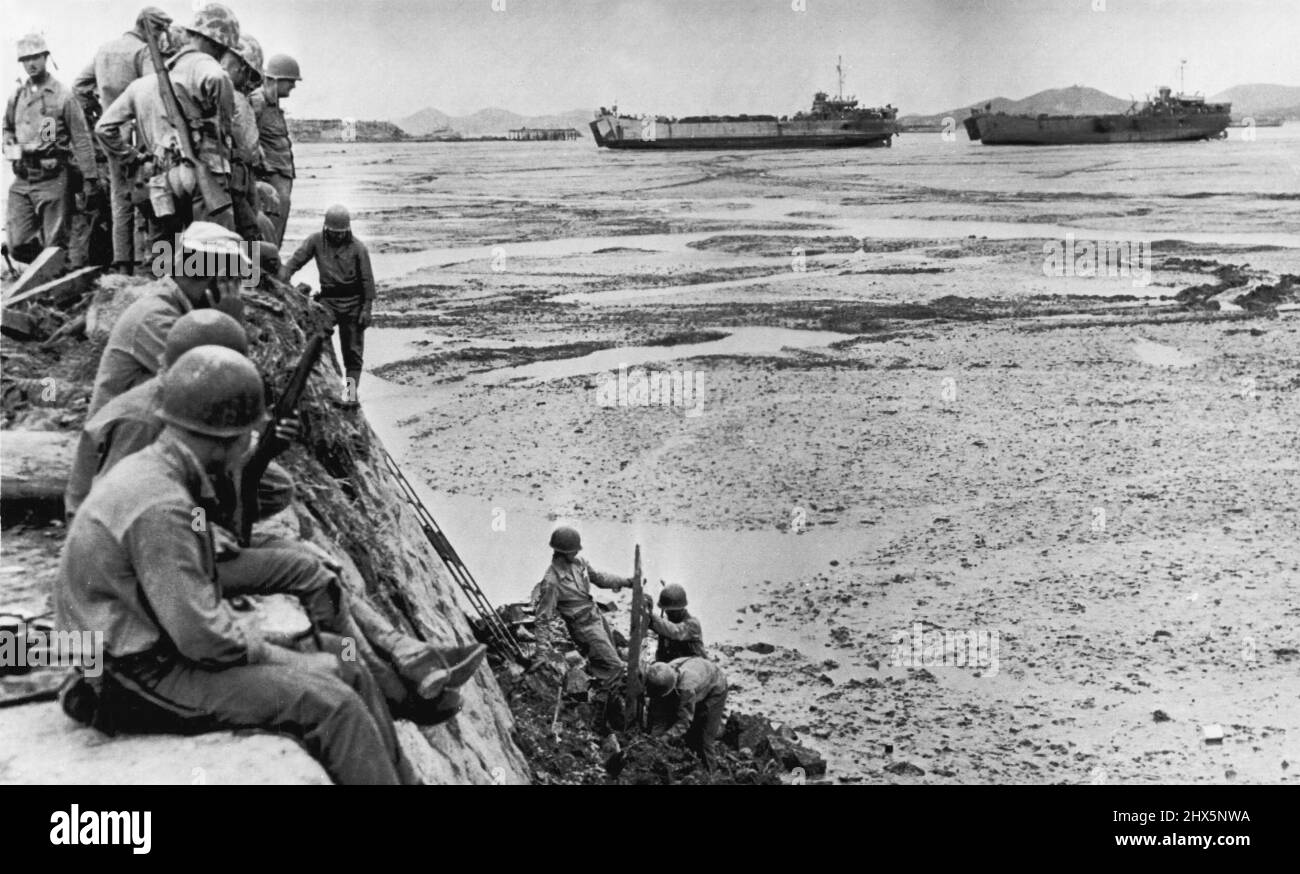 Waiting For High Tide -- Marines on Inchon sea wall watch comrades clear mud-marooned landing stage after low tides had left LST's in background high and dry. Water drops 30 feet at this point, making landing operations impossible at low tide. September 22, 1950. (Photo by AP Wirephoto). Stock Photo