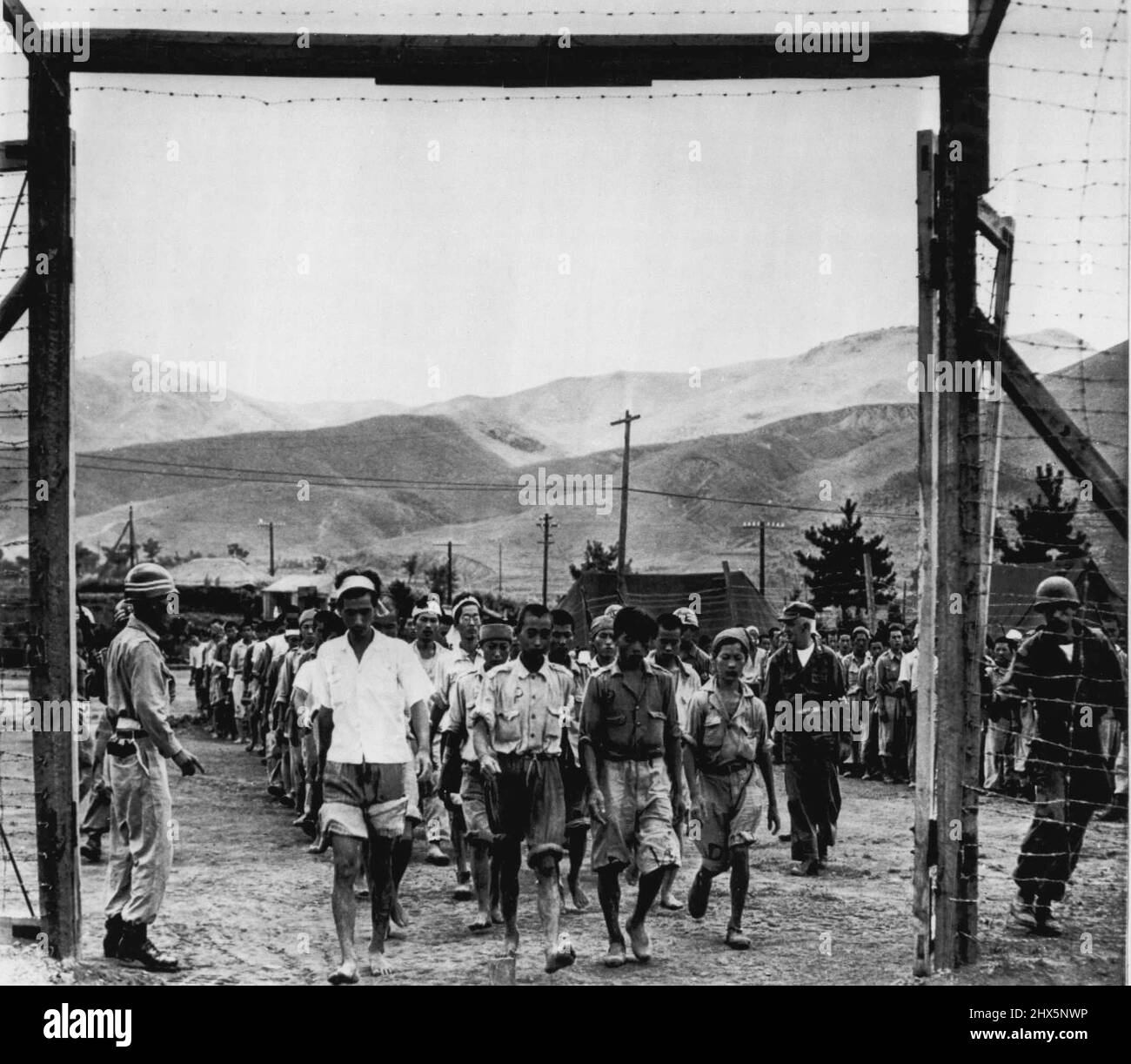 Caged For The Duration -- North Korean prisoners are marched through barbed wire gate into prisoner of war enclosure somewhere in Korea. Major John B. Hoar Jr, (second from right, MP band on arm), of Boston, Mass, camp commander looks over his charges. Maj. Hoar did similar duty during World War II. August 27, 1950. (Photo by AP Wirephoto). Stock Photo