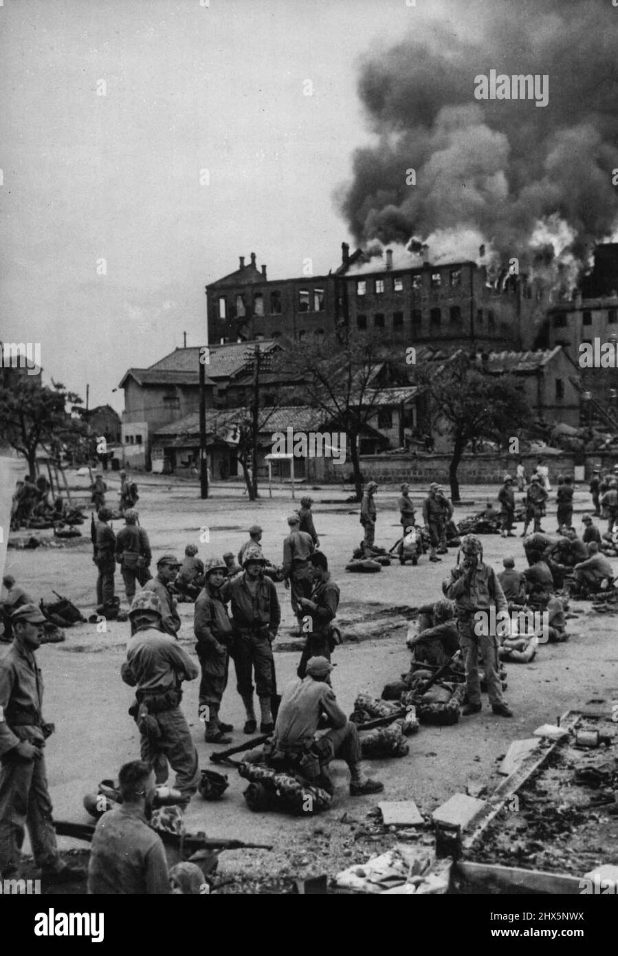 Marines At Inchon -- Troops of the American 1st Marine Division smoke chat and relax while they await orders to move forward in the United Nations drive toward enemy-held Seoul, former capital of South Korea. The Marines are shown here in Inchon, West Coast port from which the Seoul drive has been launched. In the background is a burning tobacco warehouse. (September 16, 1950. Picture received by air today). September 25, 1950. (Photo by Reuterphoto). Stock Photo