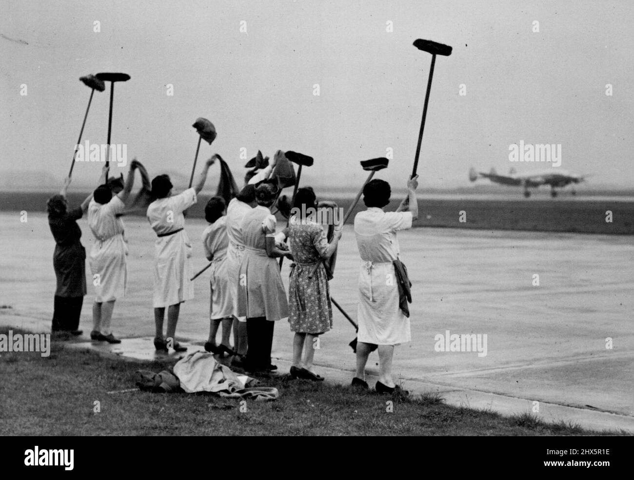 Smuts For UNO Conference -- The 'Mrs. Mops' wave 'Bon Voyage and Good Luck' with their brooms and buckets as the plane with Field-Marshal Smuts aboard soars up the runway. Before boarding the plane for New York at Heath Row, the Field-Marshal had a jest with some of the cleaners, and they all turned out to give him a good send-off. Field Marshal Smuts, the South African Premier, who has been staying in London over the week-end, left by air to-day for New York from Heath Row. He will attend the forthcoming UNO Conference and according to Major McIldowrie, his A.D.C. in an interview 'He is not Stock Photo