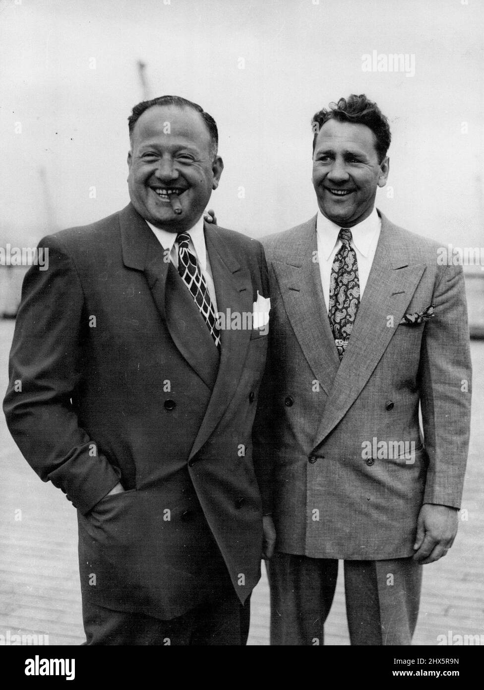 Champ Arrives. Gus Lesnevich the world light-heavy-weigh champion with Jack Solomons (with cigar) at Southampton ***** his arrival from New York in the Queen Mary. Lesnevich will take up training quarters in readiness for hit fight with Freddie Mills at White City. To keep up his strength during his stay he has brought tins of tennis and fruit juice. July 2, 1948. (Photo by Mirror Feature). Stock Photo