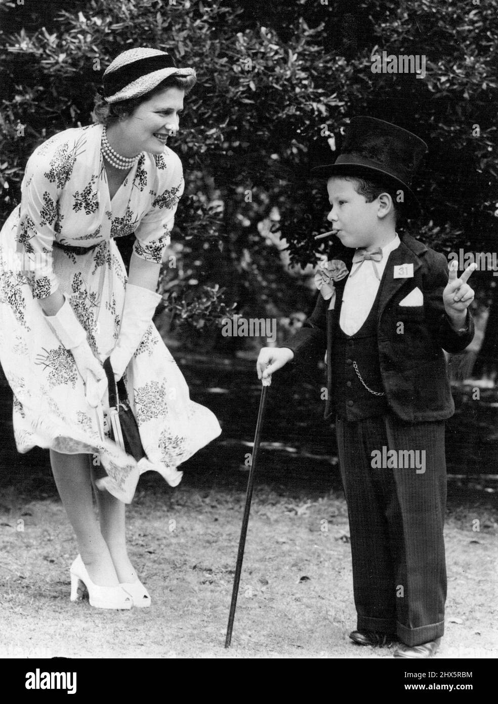 Young Adrian Wilmshurst stopped the show with his impersonation of Sir Winston Churchill at the Hastings and Rye Conservatives' garden fete at St. Leonards today. Smiling at Adrian is Mrs. Christopher Soames, the Prime Minister's daughter, who oped the fete. August 8, 1953. (Photo by Daily Mail Contract Pictures). Stock Photo