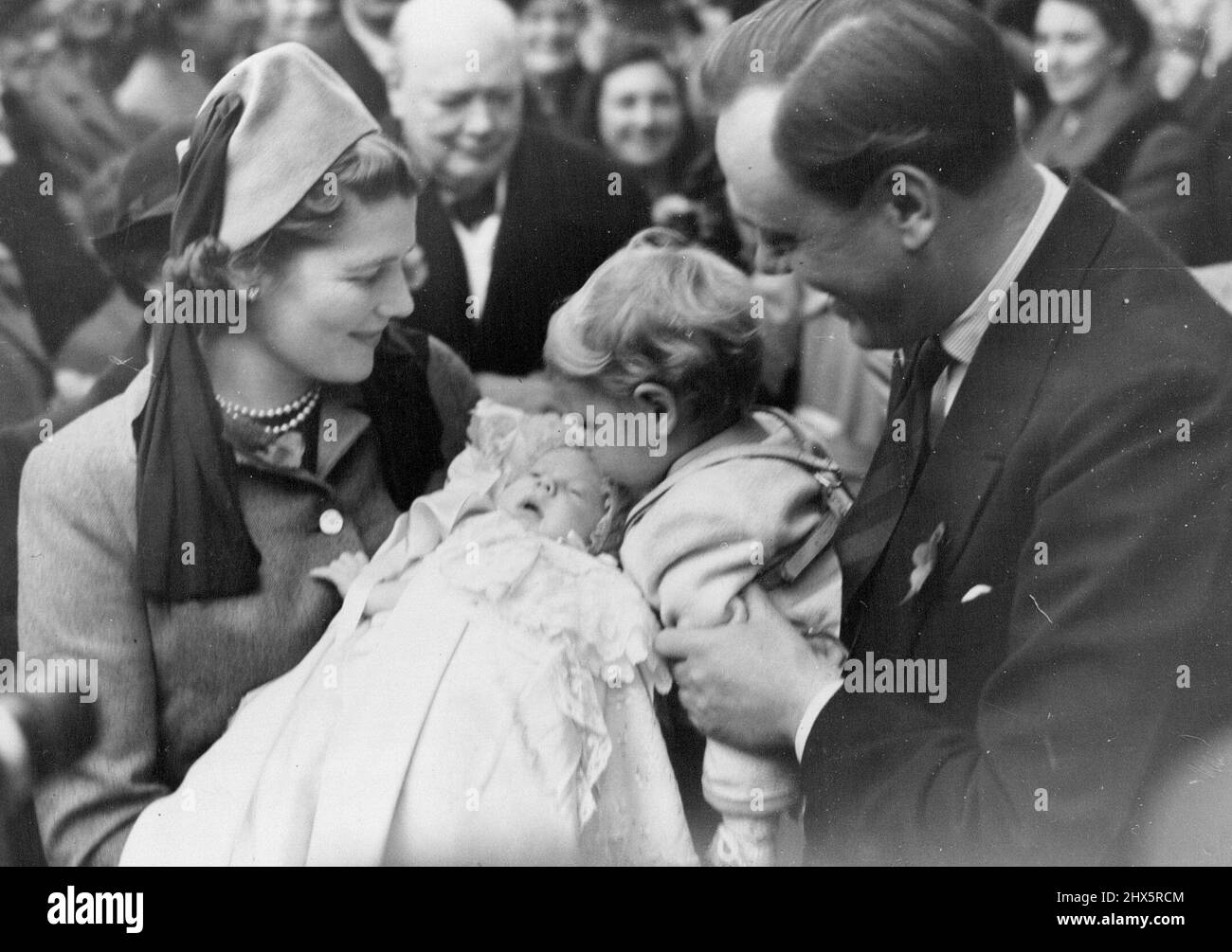 Mr. Churchill's Grandchild Christened -- Mr. Winston Churchill (in background) looks on as little Nicholas Soames kisses his baby sister Emma Mary, who is held by Mrs. Christopher Soames, formerly Miss Mary Churchill. Captain Soames is soon with his wife. Mr. Winston Churchill paid a visit to this Sussex village to attend the christening ceremony of his sixth grandchild, Emma Mary, infant daughter of Mr. and Mrs. Churchill's daughter, Mary, wife of Captain Christopher Soames. Captain Soames is prospective Parliamentary candidate of Bedford. November 6, 1949. Stock Photo