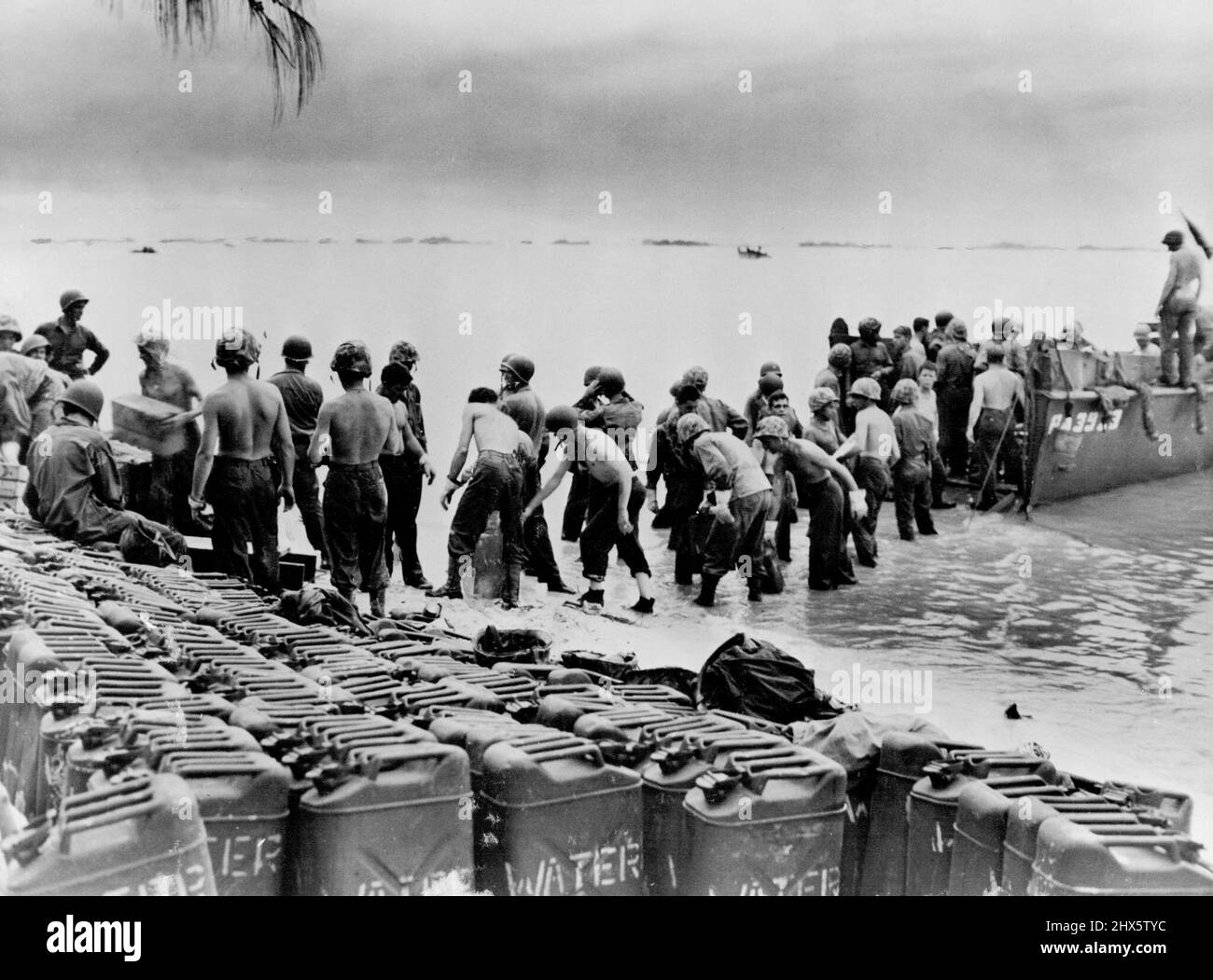 Bucket Brigade - These Marines line up, on the beach on Saipan Island, to speed the unloading of supplies and water cane. Row on row of cans filled with much needed water await transportation to interior. U. S. ships and landing craft stand by to bring in supplies, and safeguard beach. July 13, 1944. (Photo by Official U. S. Marine Corps Photograph) Stock Photo