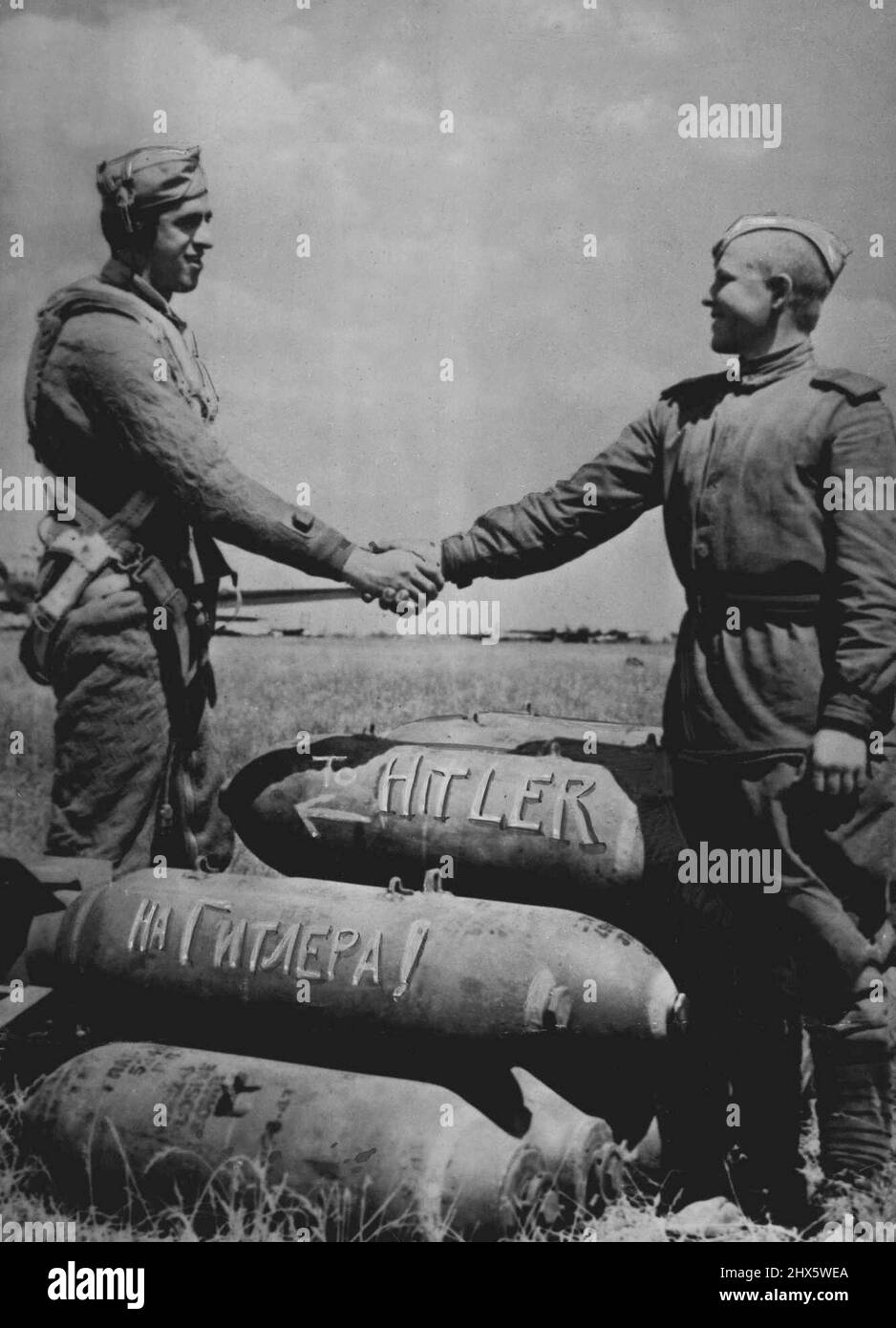 American And Russian Soldiers Shake Hands Over Bombs For The Enemy -- At an air base in Russia used by American aircraft, a U.S. and Red Army soldier shake hands over a pile of bombs addressed to the enemy. The Russian words 'to Hitler' are painted on a bomb under one bearing the English spelling American aircraft have used bases in Russia since June 2, 1944, when Flying Fortresses left a base in Italy, bombed German targets in Rumania, and combined to new airfields in Russia prepared to receive Stock Photo