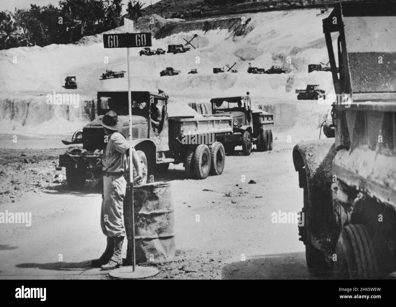 Trucks Speed Crushed Coral For Saipan Superfort Base -- An American military policeman gives the go signal to ten-wheeled trucks, carrying crushed coral from a mountain quarry on Saipan, during construction of the B-29 Superfortress base from which attacks are now being launched against Tokyo. Power shovels (background). and more than 100 trucks worked day and night to build the huge airstrips within five months after Saipan in the central Pacific Marianas was captured from the Japanese. The fir Stock Photo