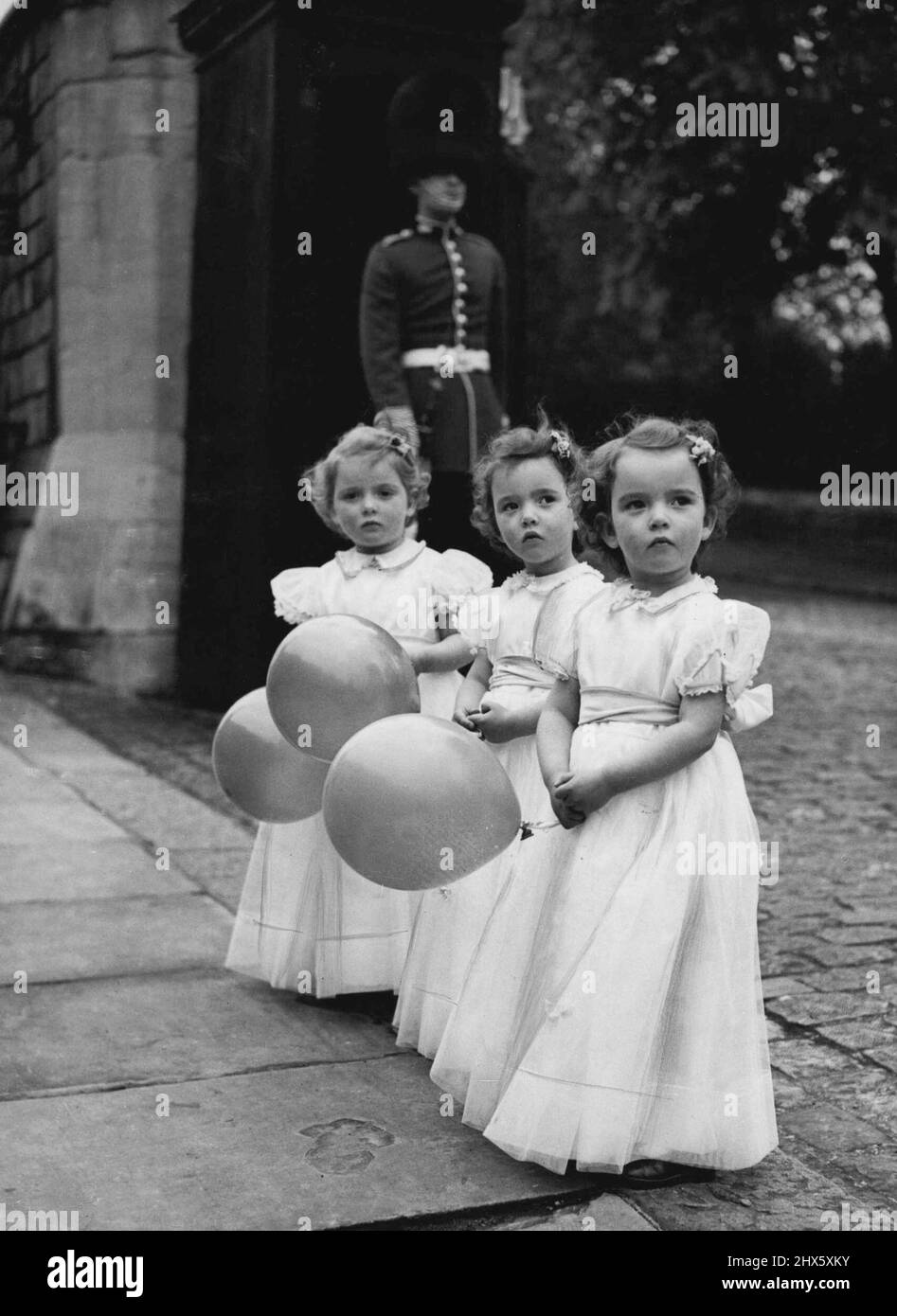 Bridesmaid' Triplets -- Three-year-old triplets (left to right) Karen, Elizabeth and Susan Stewart make this charming picture as they are 'all dressed up' for a children's fashion display at Windsor, Berks. They are wearing net over tafetta bridesmaids' dresses with coloured sashes, designed by Caleys.The children are the daughters of Johnny Stewart, the comedian. April 26, 1952. (Photo by Reuterphoto). Stock Photo