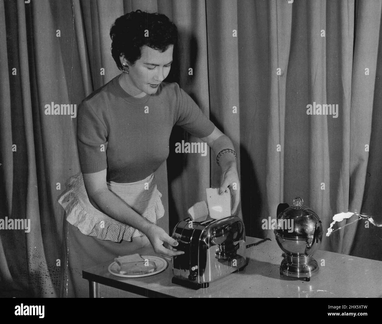8am: The coffee's bubling in her electric percolator while she slips the bread into the toaster. No danger of serving husband with burned toast either. This new design toasts to a crisp brown, then pops it out ready to serve. May 11, 1954.;8am: The coffee's bubling in her electric percolator while she slips the bread into the toaster. No danger of serving husband with burned toast either. This new design toasts to a crisp brown, then pops it out ready to serve. Stock Photo
