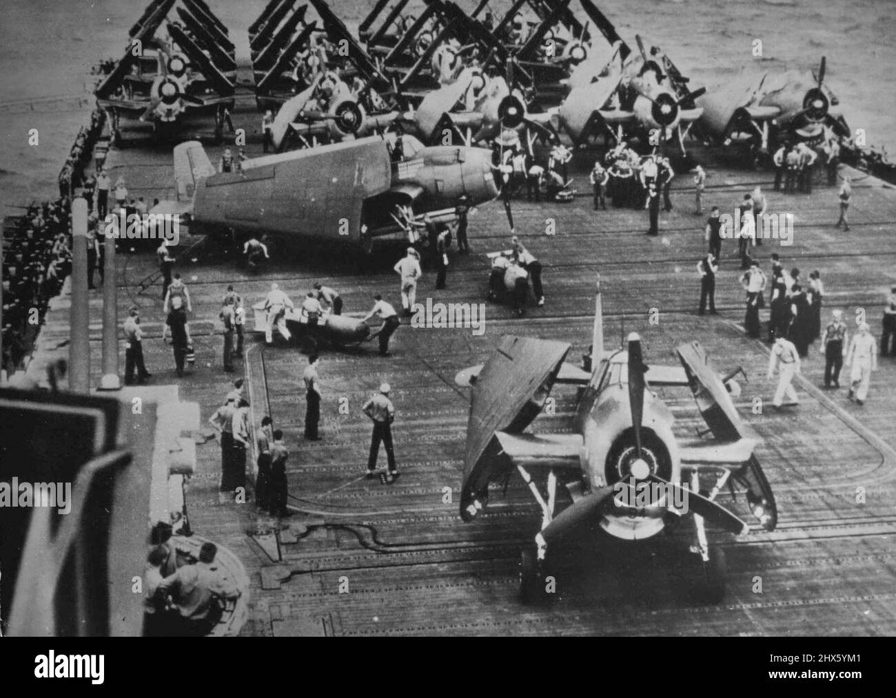 Loading U.S. Torpedo Bombers For Strike Against Japanese -- Torpedoes are loaded aboard an Avenger bomber, which is about to take off the flight deck of a U.S. Navy aircraft carrier for a strike against the Japanese in the Pacific. Other planes, part of the Navy's Carrier Air Group Two, stand ready on the deck with wings still folded to save space. Carriers like this one were part of the hard hitting American and Australian naval forces which, in dealt simultaneous battles late in October, 144, Stock Photo
