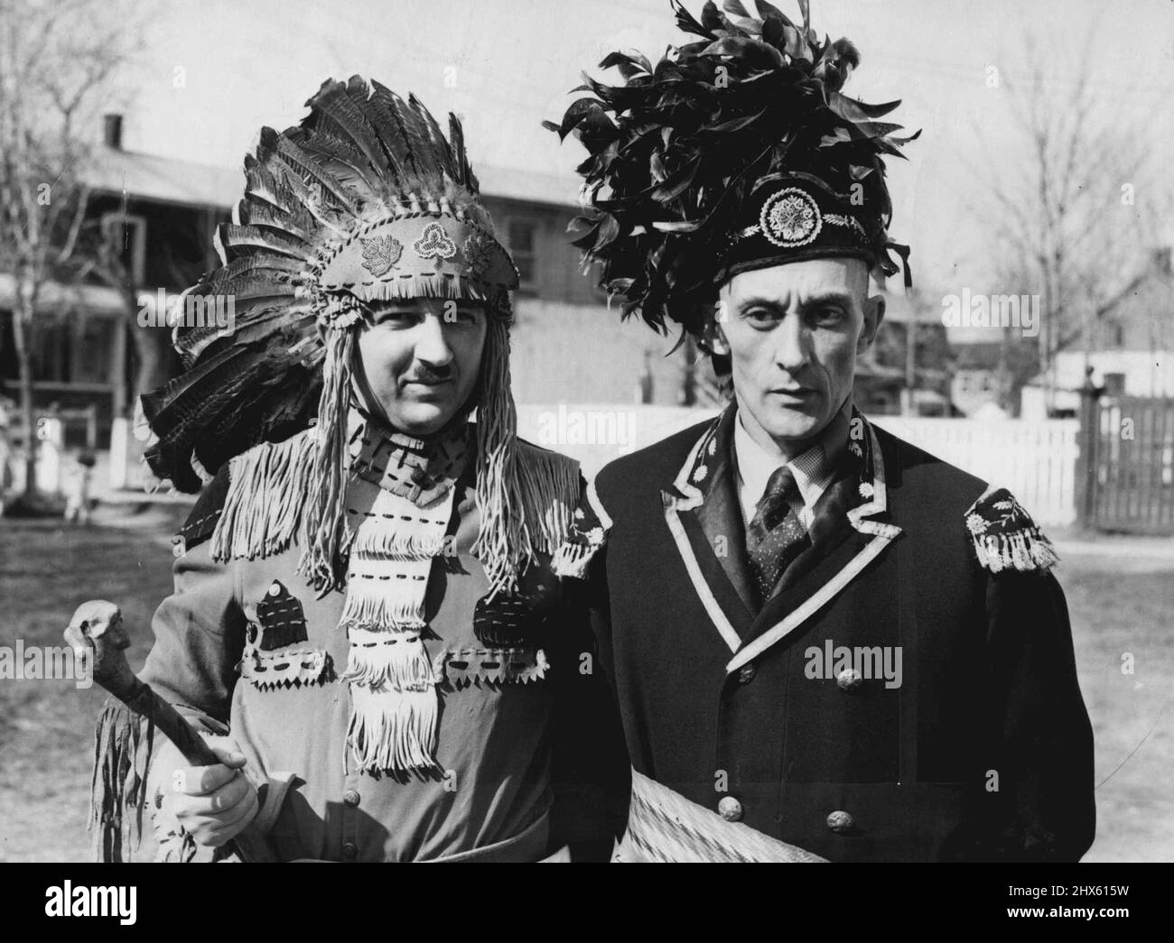 Huron Indians To Greet king And Queen -- These pictures, of the Huron Indians, the oldest tribe in North America, were made at their reservation near here, as they spruced up their ceremonial bonnets in preparation for their ceremony to greet King George and Queen Elizabeth. This close up of two Indians in war Regalia, shows Jules Sioui, (left), and Arigene Sioui. The warrior on the left is wearing the ancient Huron dress, while the brave on the right is wearing comparatively modern head-dress a Stock Photo