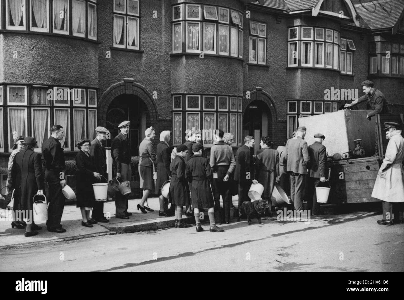 Troops To The Help Of Flooded London -- The long queue carrying every sort of utensil wait their turn as the Army water wagon brings their much needed supply. A picture from Clapton, London. Soldiers bringing with them many hundreds of mobile water tankers have now been called in to help in the flooded districts of London where large areas are completely without a domestic water supply owing to the rising flood waters overrunning the reservoirs and works. March 17, 1947. ;Troops To The Help Of Stock Photo