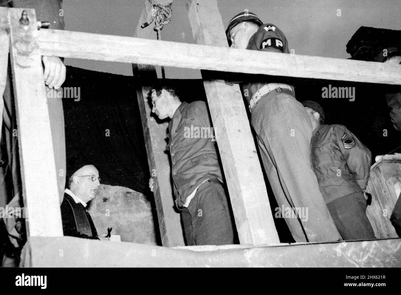 Three German Civilians Executed-First Pictures -- A Catholic priest kneels in prayer before Mathias Gierens, delivering the last sacrements, before the black hood is placed over his head and the executioner carries out sentence. Three German civilians, the first war criminals to be tried in Germany, were hanged at dawn on June 29, at the Military prison at Rhinebach. All three were found guilty of the murder of an American airman who parachuted to earth from his blazing bomber last August 15. T Stock Photo