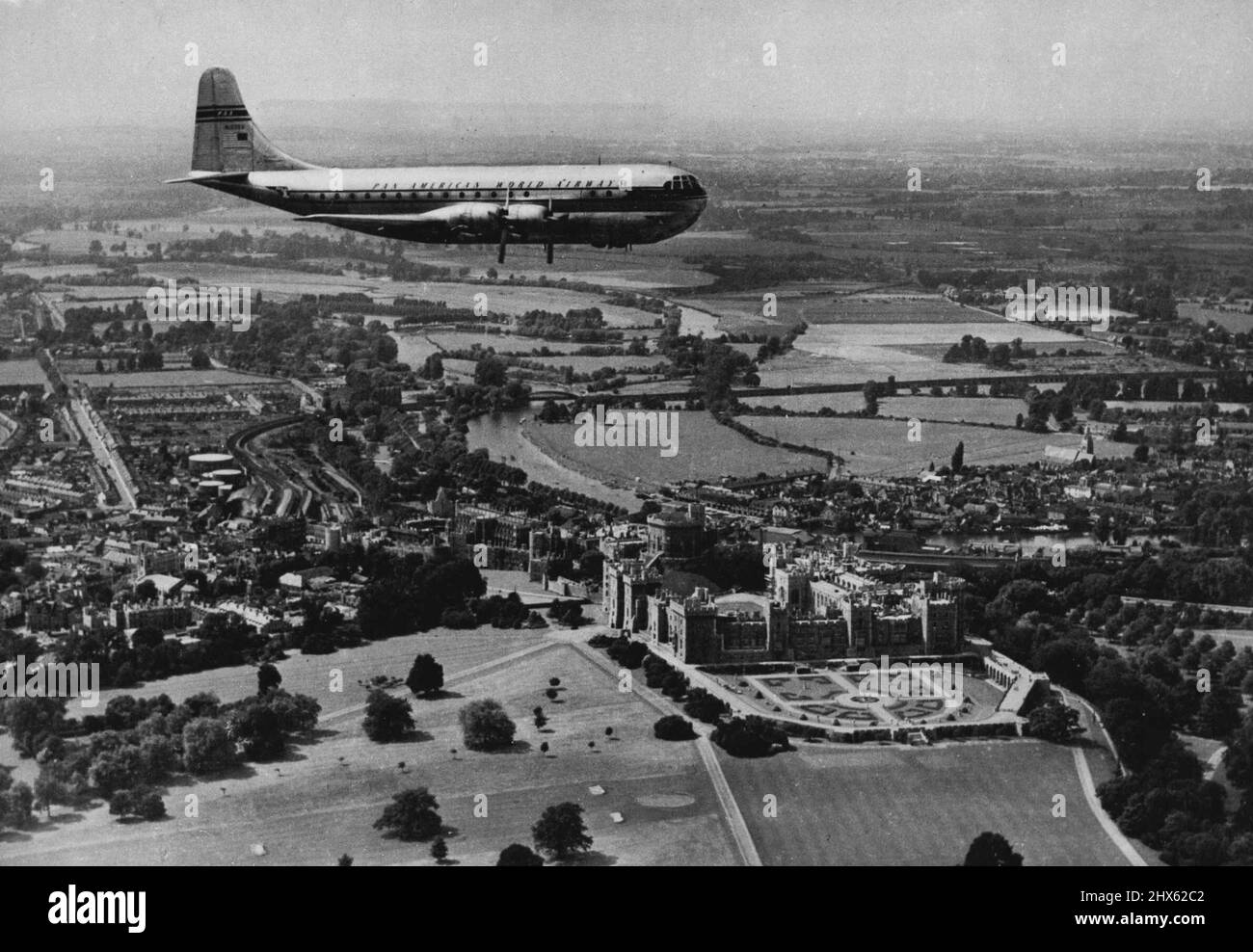 The Span of A Thousand Years Nearly a thousand years of history glides under the majestic wings of this Pan American 'Stratocruiser', world's largest aeroplane in commercial service, as she passes over Windsor Castle en route to London Airport from New York. Beneath the 'Stratocruiser' the Castle - a Royal residence since the days of William the Conqueror (although it was built mainly by Henry III) - spreads its gracious grey bulk on the banks of the River Thames, winding through the chequered B Stock Photo