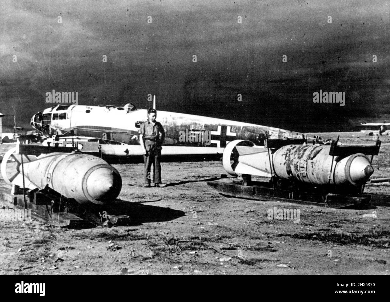 Putting The Skids Under Them — Hero ere heavy bombs on wooden skids or sleds on which, they were moved across the aerodrome at Benina, near Benghazi. They were abandoned by enemy forces in their retreat westwards. The bomber In back.-ground appears to be a Heinkel He-111. March 3, 1943. (Photo by British Air Ministry Official Photograph). Stock Photo
