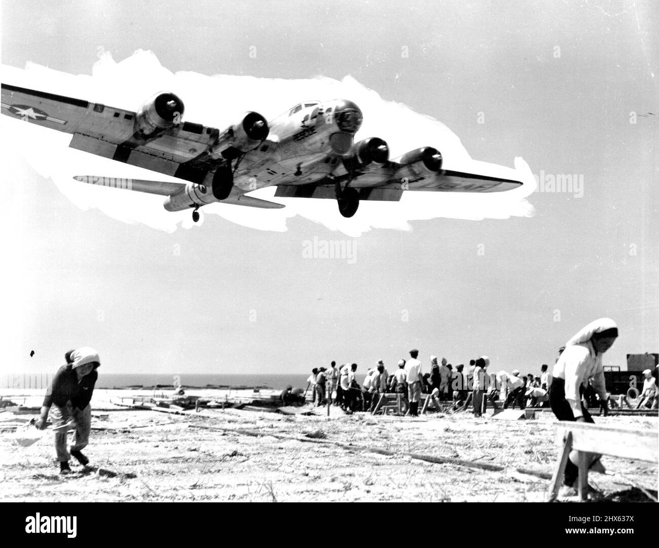 Returns From Search Mission An Airbase In Japan - A huge the Third Air Rescue Squadron roars in low over the heads of Japanese laborers who continue working with an air of complete indifference. The giant search plane makes long-range flights over the ocean between Japan and island bases when Far East Air Forces crew members have been forced to make emergency ditchings at sea. When survivors are located, the SB-29 is capable of launching a 12-man life boat, complete with survival gear for a two Stock Photo