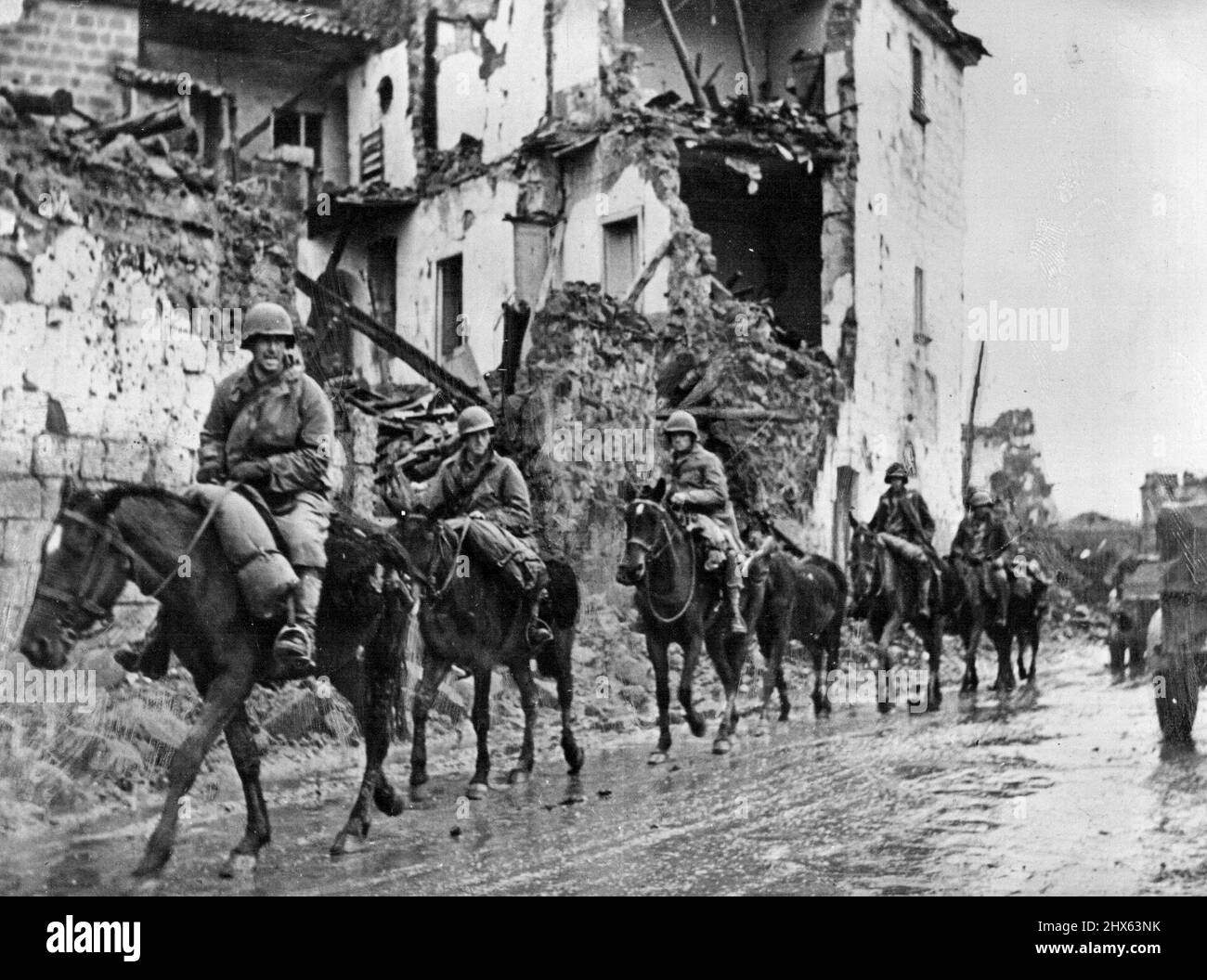 New U.S. Cavalry Advance in Italy: A U.S. cavalry detachment of the Allied Fifth Army passes through a shell-torn Italian town. The mounted men are known as Provisional Mounted Reconnaissance troops and were organized early in the Allied campaign in Italy. They have proved effective in destroying German machine gun nests and artillery emplacements inaccessible to motorized forces. January 10, 1943. (Photo by U.S. Office of War Information Picture). Stock Photo