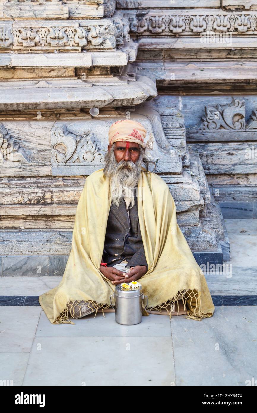 Sadhu sitting cross-legged by a typical carved wall in the Jagdish Temple, a Hindu temple in Udaipur, Indian state of Rajasthan, India Stock Photo