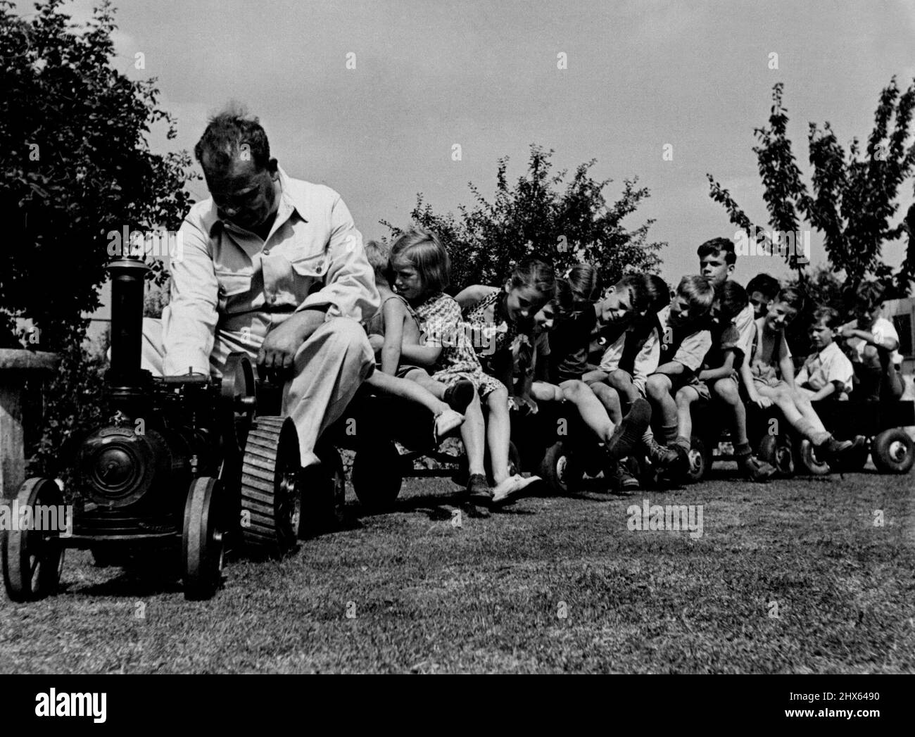 Model Steam Traction Engine -- The model steam tractor is being shown at the Model Engineers Exhibition which opened yesterday in London. Mr. R.G. Hammett who built it, is seen giving a ride to fourteen youngsters round the garden of his home at Den son-road, Boxleyheath. August 18, 1949. Stock Photo