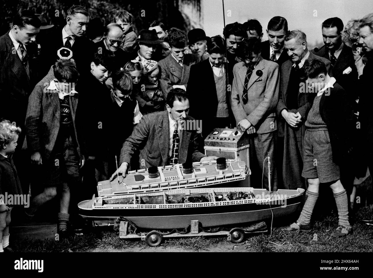 This Queen Mary Has Radio Control -- Ashore the radio controlled Queen Mary attracts a large crowd as Mr. Pyser removes the 'upper deck' at prince of Wales' pond, Blackheath. Model boat enthusiasts and pool side strollers got a surprise the other day when they saw a perfect scale model of the liner 'Queen Mary' ploughing steadily across the 'Ocean' of prince of Wales Pond, Blackheath. The ship turned, went astern and even hove to off shore, with only the radio antennae to give a clue as to how i Stock Photo