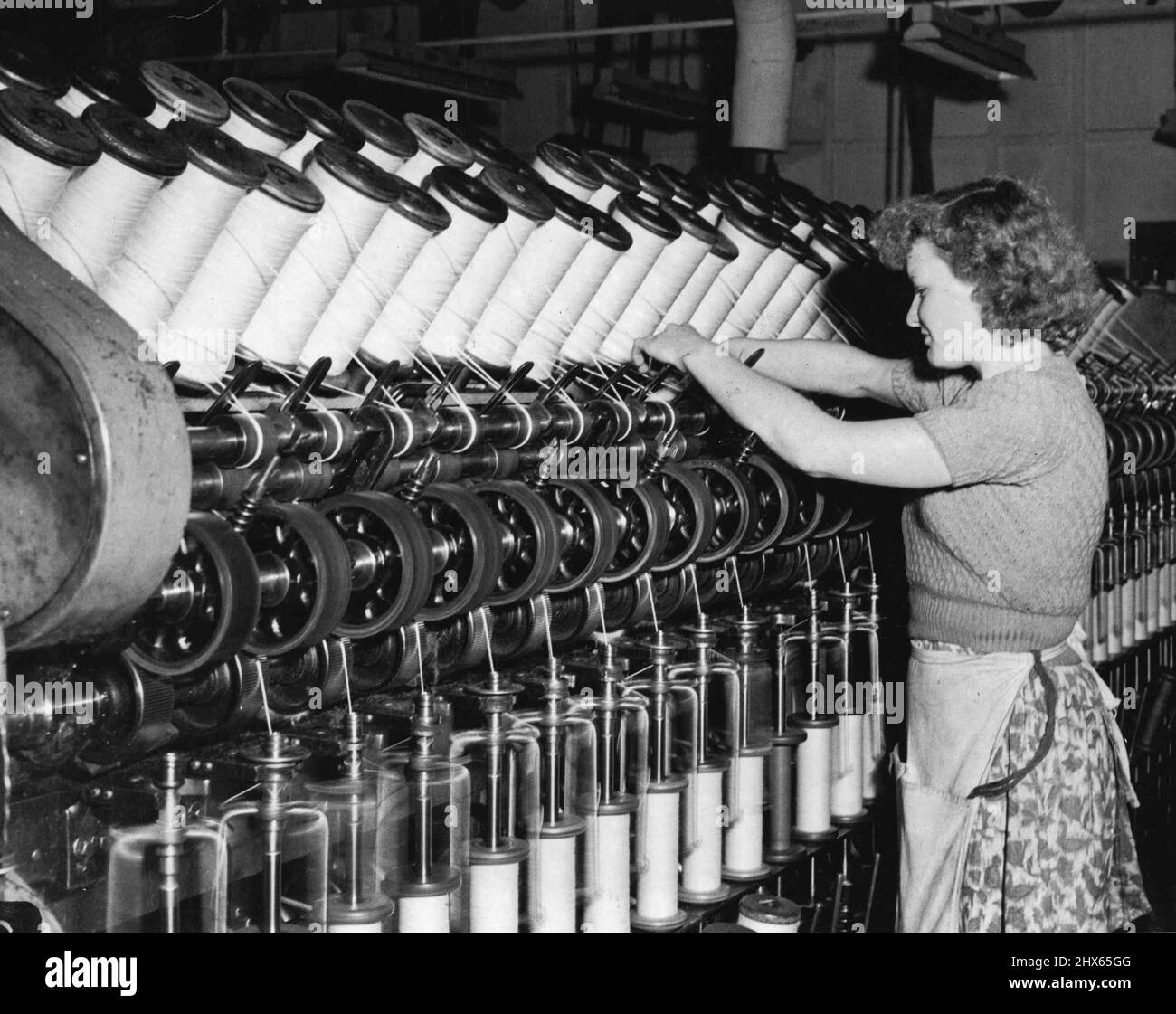 Sheep Supp. - At John Vicars Pty Ltd Marrickville. The roving operation in the drawing dept. Here the operator is fitting a full spool in the machine which draws the combed wool into fine slivers ready for spinning. May 28, 1952. (Photo by Frank Albert Charles Burke/Fairfax Media). Stock Photo