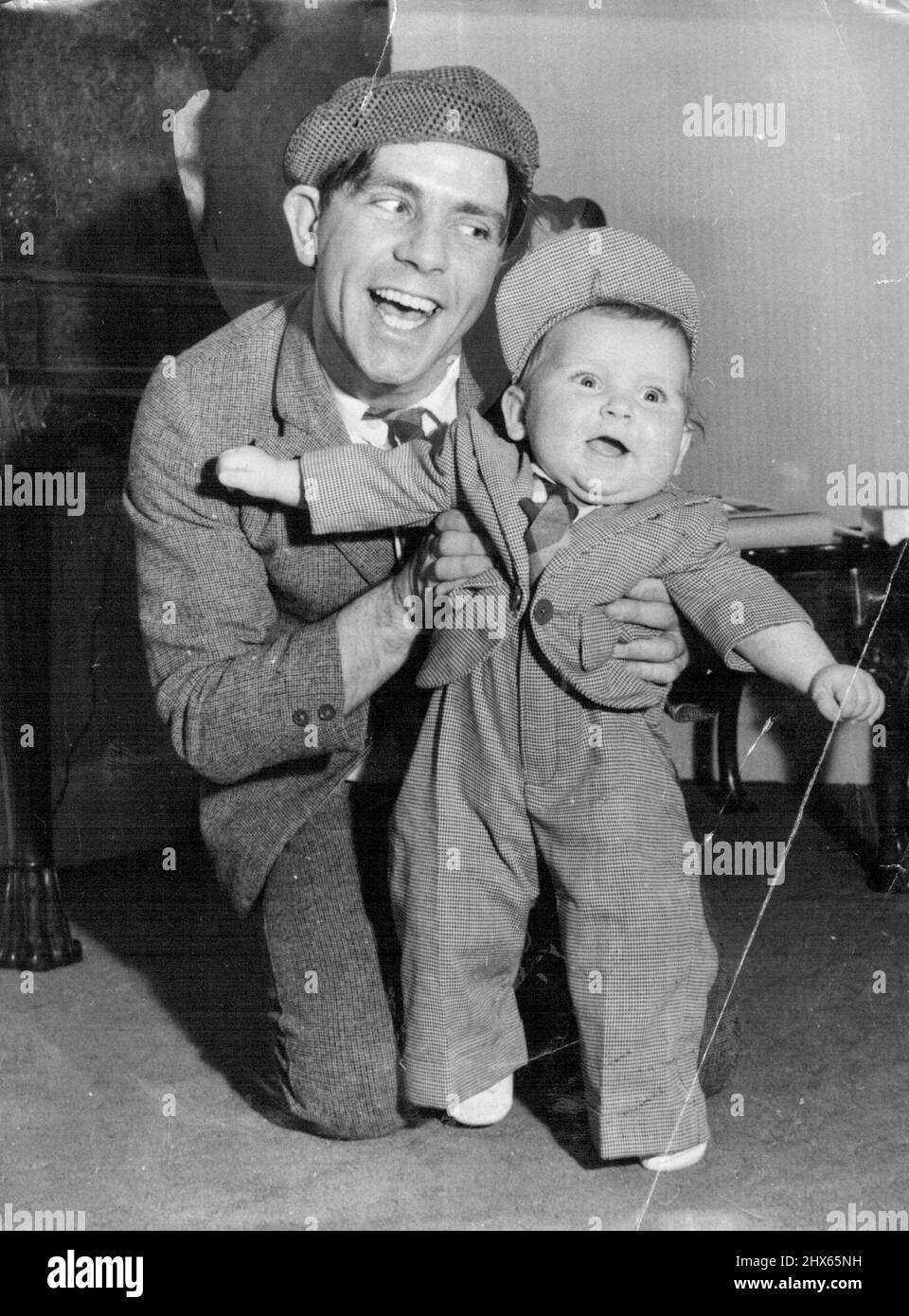 Christmas - I'm Ready For It - Bubbling over with Christmas fun and ready to throw him self about like father is Nicholas, his months-old son of comedian Norman Wisdom, who's restraining his effervescent youngster at the Empress Hall, London. Nicholas, about to celebrate his first Christmas, wears one of his presents - a suit just like dad's made for him by members of the 'Sinbad the Sailor on Ice' Show, in which Norman stars at the Empress Hall. December 23, 1953. (Photo by Reuterphoto). Stock Photo