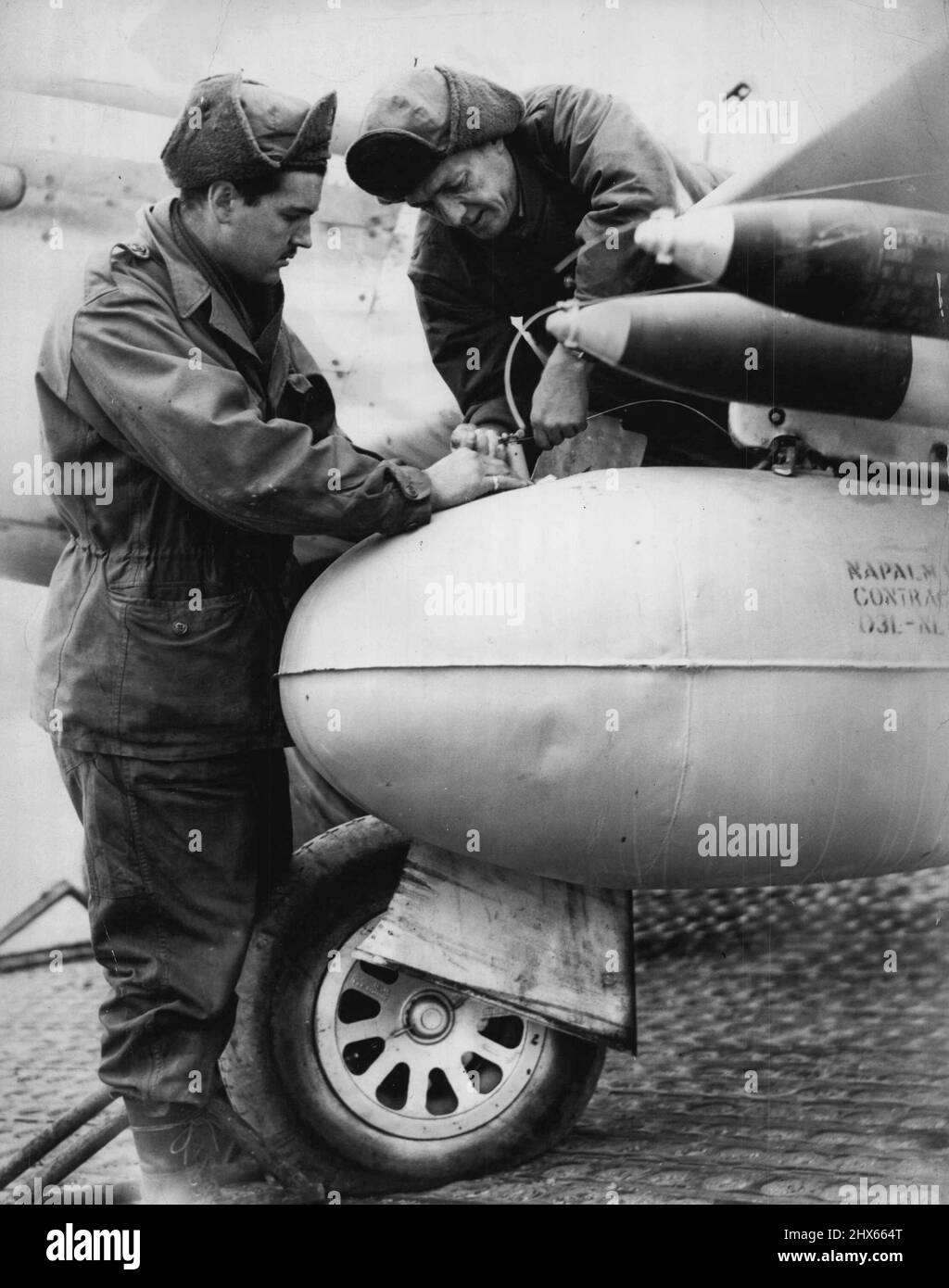 Deadly Napalm bomb being fitted wing rack of Mustang before aircraft took off to attack enemy troops. L to R Lac Ron Ecclis, of Chelsea, Melb, Sgt, Ray Burgum, of Maleny, Qld. December 29, 1950. Stock Photo