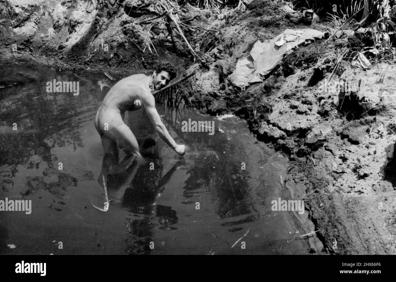 Pte. Sal Corona of California uses a bomb crater as a swimming pool. The crater is on the main strip at Buna and, when the photo was taken, Japanese were only 100 yards away. January 15, 1943. (Photo by Department of Information, Commonwealth of Australia). Stock Photo