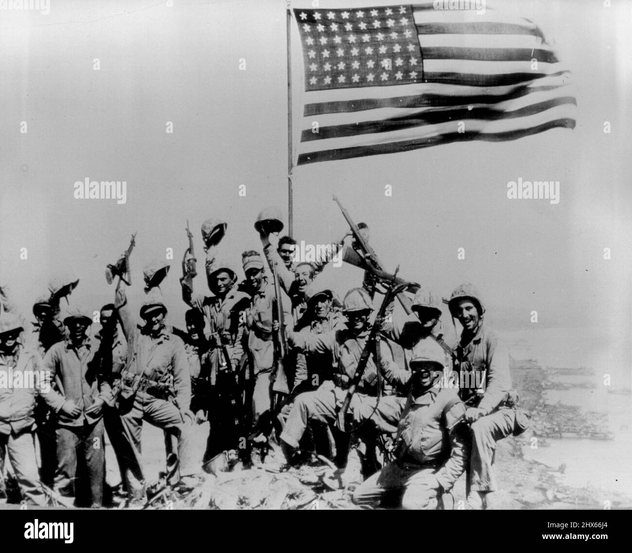 They Put U.S. Flag Atop Suribachi - Marines of the 28th Regiment, 5th Division, wave from in front of the American flag they put atop Suribachi, Iwo Jima’s volcano, after a bitter uphill battle with the Japanese in caves and pillboxes on Iwo Jima’s natural fort. February 27, 1945. (Photo by Joe Rosenthal, AP). Stock Photo