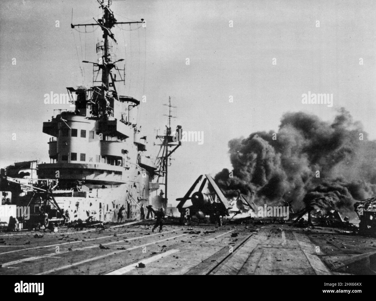 Suicide In Vain -- After the Jap plane hit, sailors rush across the flight deck with fire-fighting equipment to extinguish the blaze. Using one of its last resorts to stop the advance of the British and Americans, Japan sent pilots out on suicide missions during the recent Okinawa campaign. This British Pacific fleet carrier was the victim of a crash-diving Jap suicide plane during recent operations off the 'Sakishima Islands, a few hundred miles from the Japanese Mainland, when the British were Stock Photo