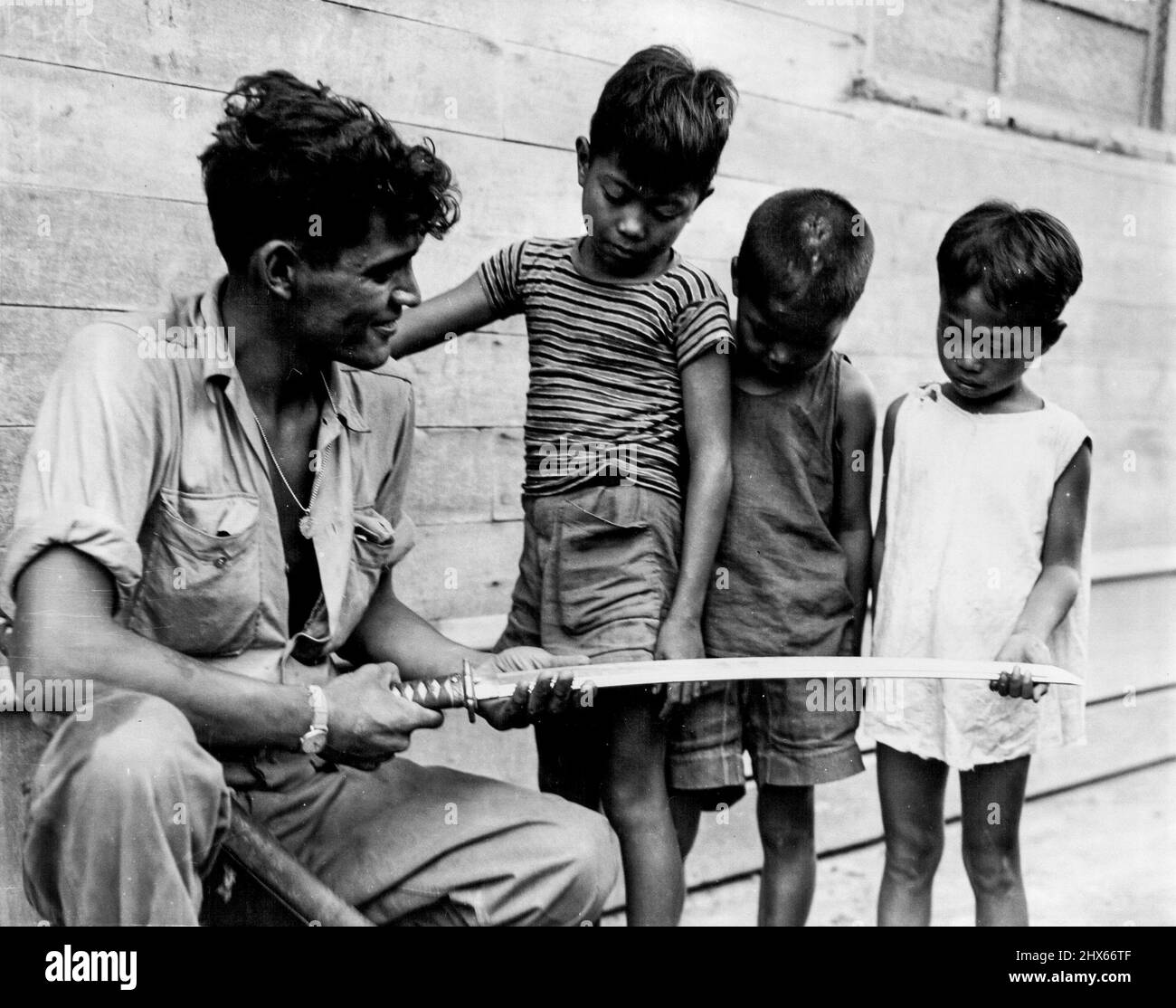 Hero Worship -- Filipino children solemnly inspect a Samurai sword that Private First Class Cornelius A. Lubo, Syracuse, New York, took from a Jap officer after slaying him and his sixteen-man patrol at Palo Bridge, Palo, Leyte Island. December 11, 1944. (Photo by USA Signal Corps Photo). Stock Photo