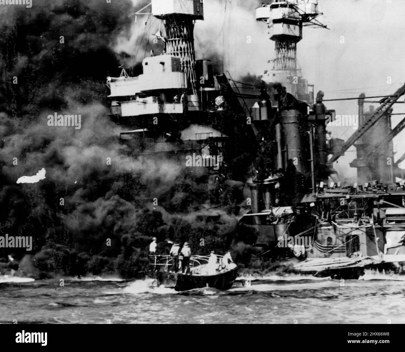 A small boat rescues a seaman from the water near the blazing U.S.S. West Virginia, while rests on the bottom after the warship was ***** by Jap bombs and Torpedoes during the attack of Pearl Harbor, December 7th, 1941. Smoke rolls out from amidships, showing where the most extensive damage occurred. Note two men ***** aboard (on bridge, upper center). Beyond the West Virginia, is the battleship, U.S.S. Tennessee. This photo was just released by the Navy department in Washington. February 4, 194 Stock Photo