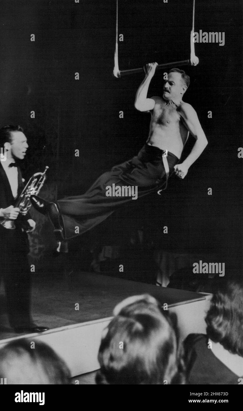 Darryl Zeuck flexes his muscles as he attempts unsucessfully to chin the bar on trapeze one arm trumpet player Joe Vincent. Zanuck's display climaxed an Oriental Party in Swank Hollywood nightclub (Ciro's ). January 18, 1954. (Photo by Associated Press Photo) Stock Photo