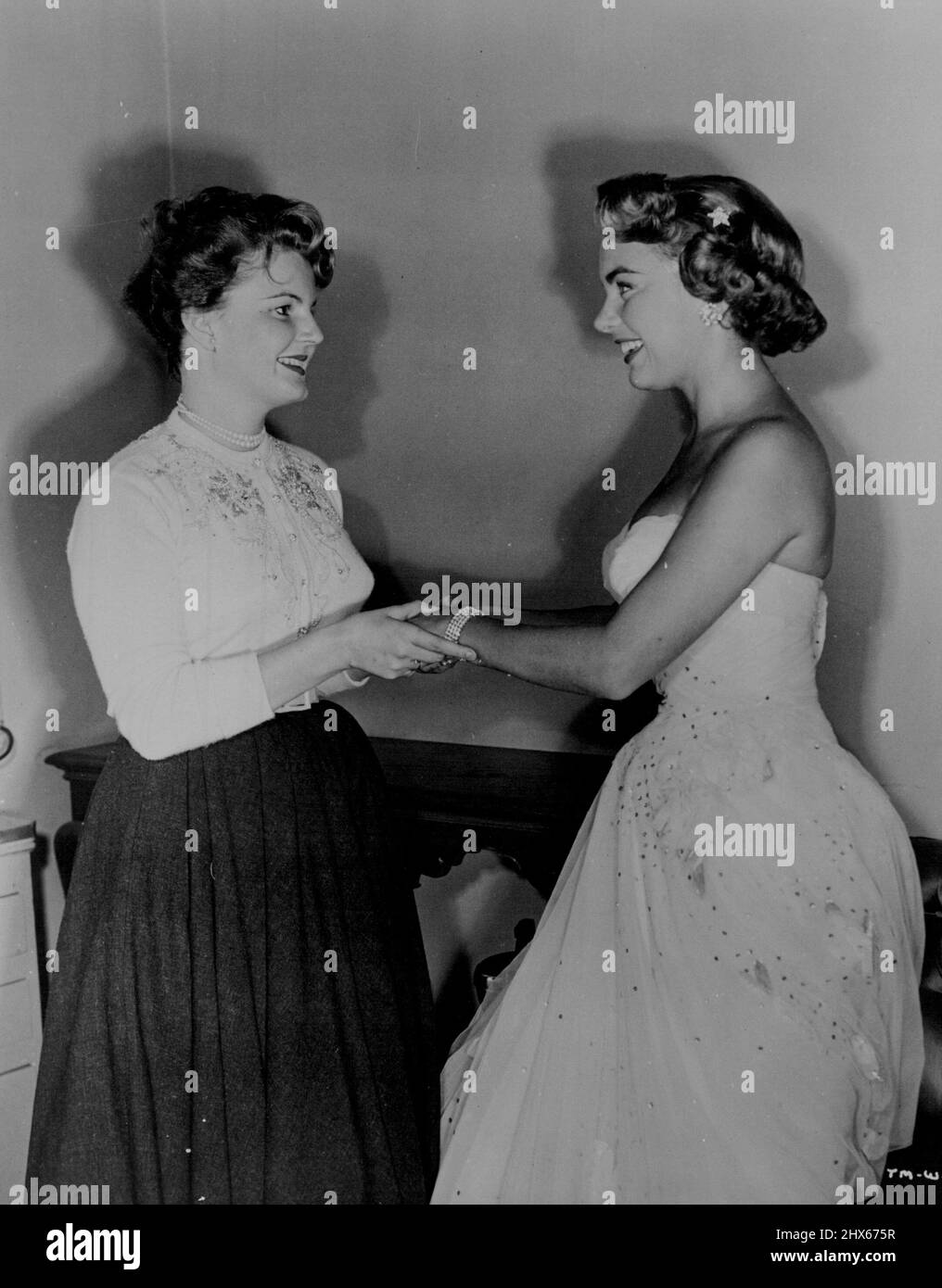 Attractive, talented Susan Zanuck, who along with Miss Moore was a member of the Hollywood troupe which entertained United Nations troops in Korea during the holidays, and the daughter of 20th Century-Fox's vice-president in charge of production, Darryl F. Zanuck, is shown greeting vivacious Miss Moore rind helping with the final touches on her stunning evening attire. December 03, 1954. Stock Photo