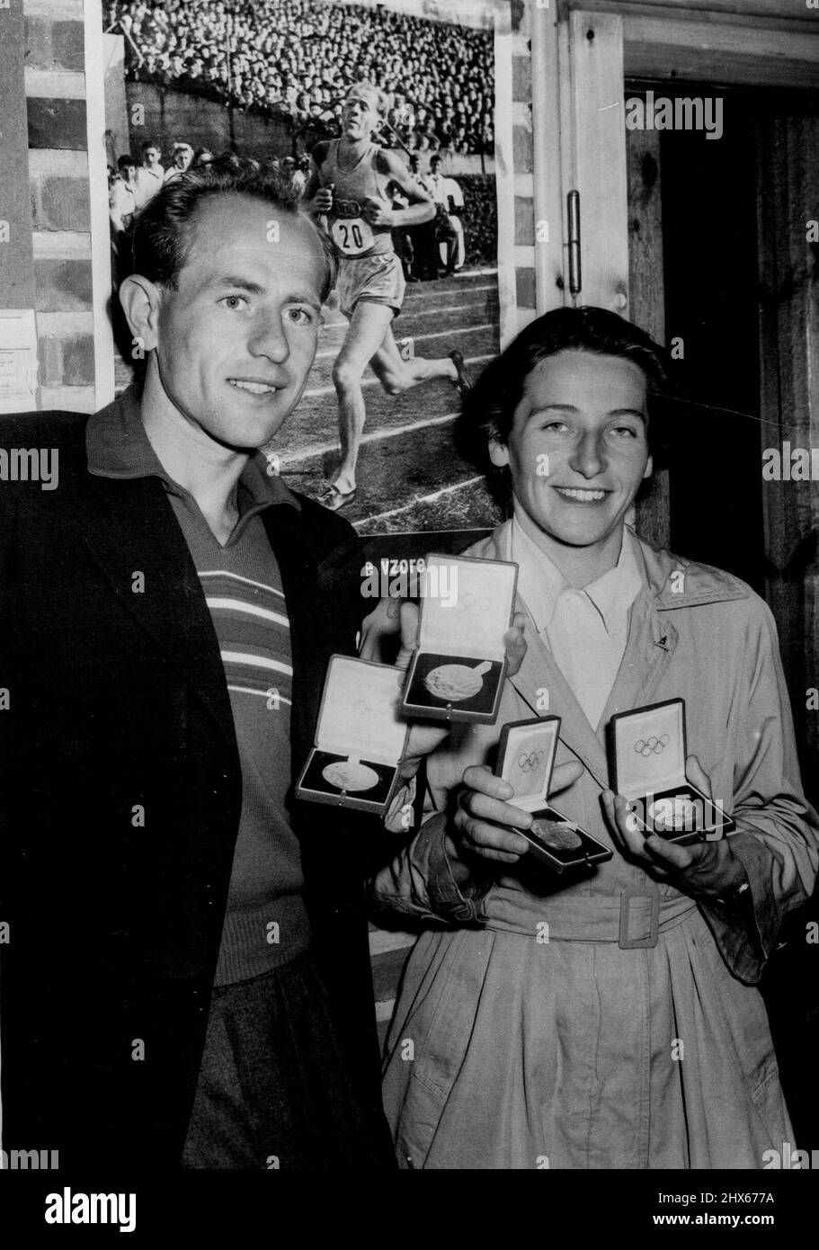 The Winning Zatopeks -- Emil Zatopek of Czechoslovakia, winner of the Olympic Games 5,000 metres, 10,000 metres and marathon, with his wife Dana Zatopkova, who won the ladies javelin event, show their four gold medals at the Otaniemi *****. In background is an Olympic action picture of Zatopek. July 31, 1952. Stock Photo