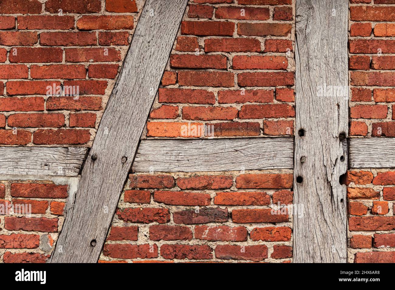 Background texture of an old timber frame wall, consisting of weathered wooden beams and red bakestone bricks, typical for half-timbered architecture Stock Photo