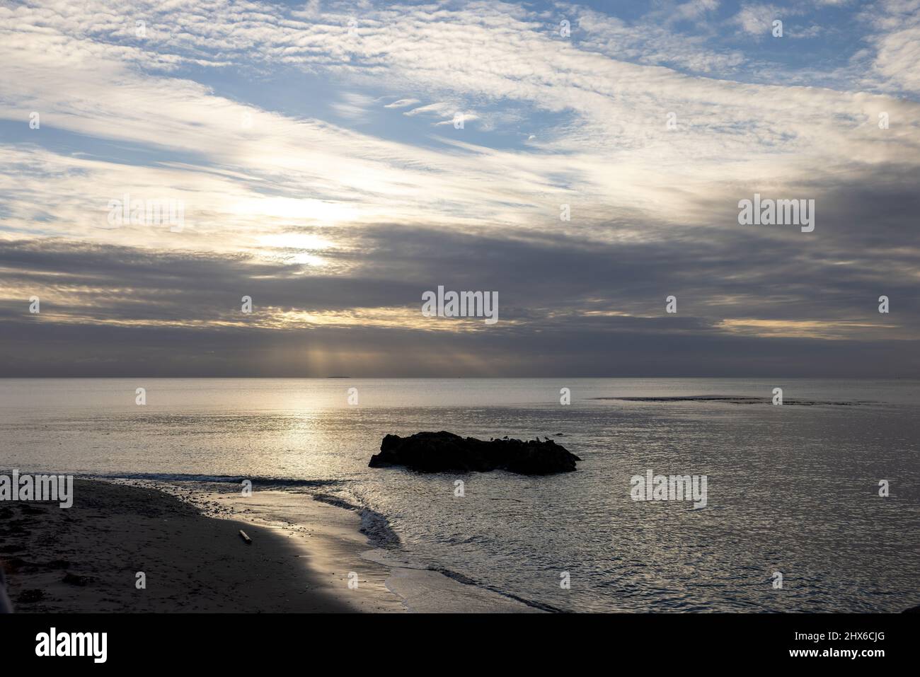 dramatic light streaming through wispy clouds over calm ocean water Stock Photo