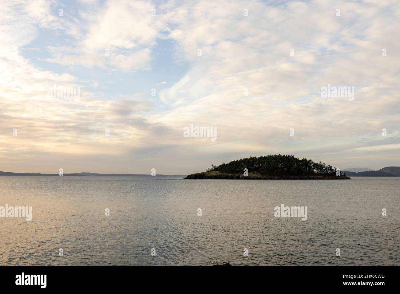 dramatic light streaming through wispy clouds reflecting in calm ocean water Stock Photo