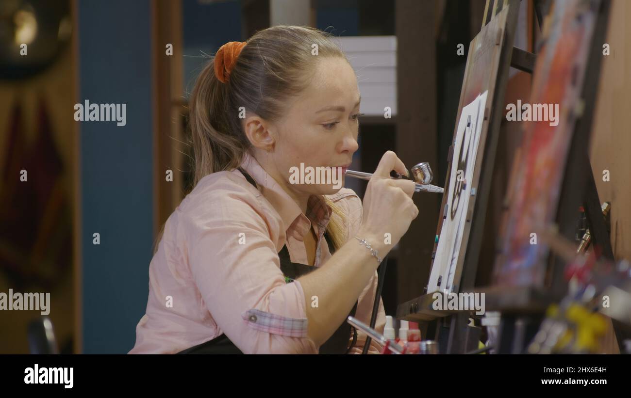 Woman artist learns to paint with airbrush with acrylic dye, paper and