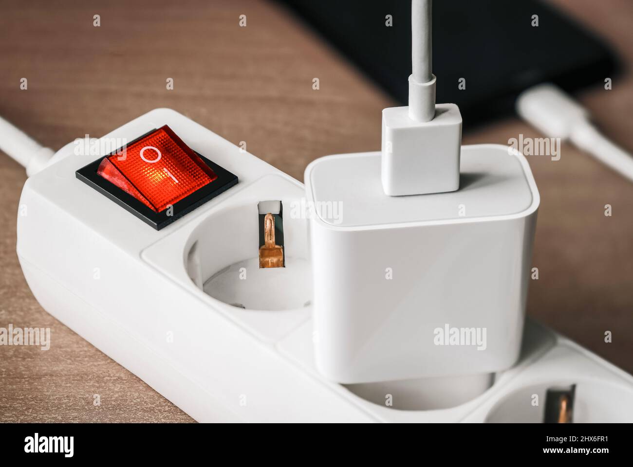 A charger adapter with a USB cable connected to a power supply with a red switch for charging a smartphone. Stock Photo