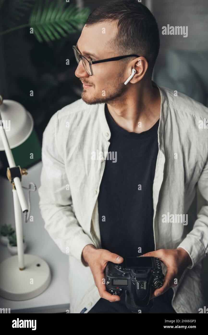 The portrait of a photographer holding the camera in his hands and looking to one side, thinking about which picture to choose. Photo indoors Stock Photo